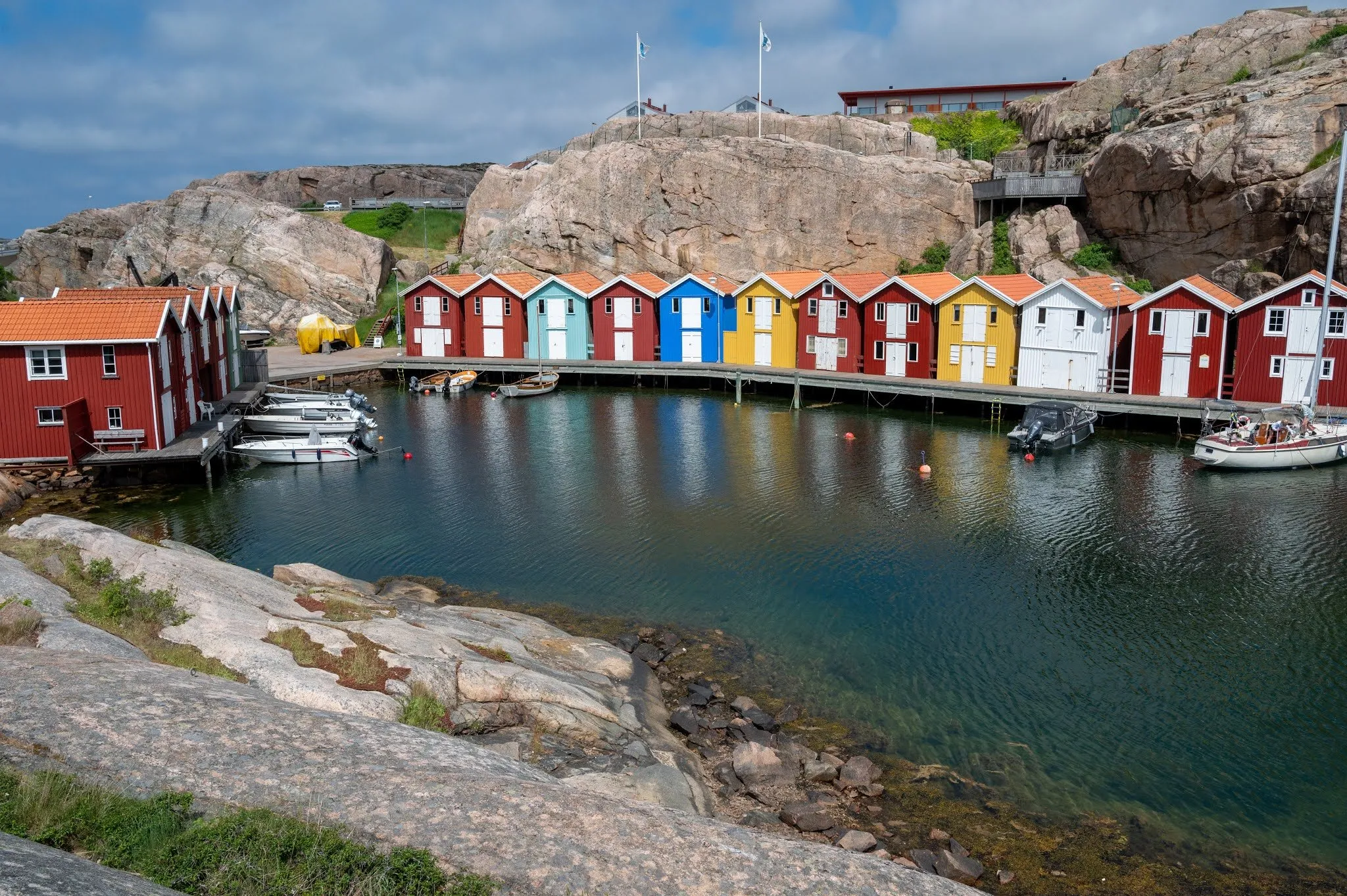 Colourful fishing huts of Smögenbryggan on a calm bay, a flat rock in front
