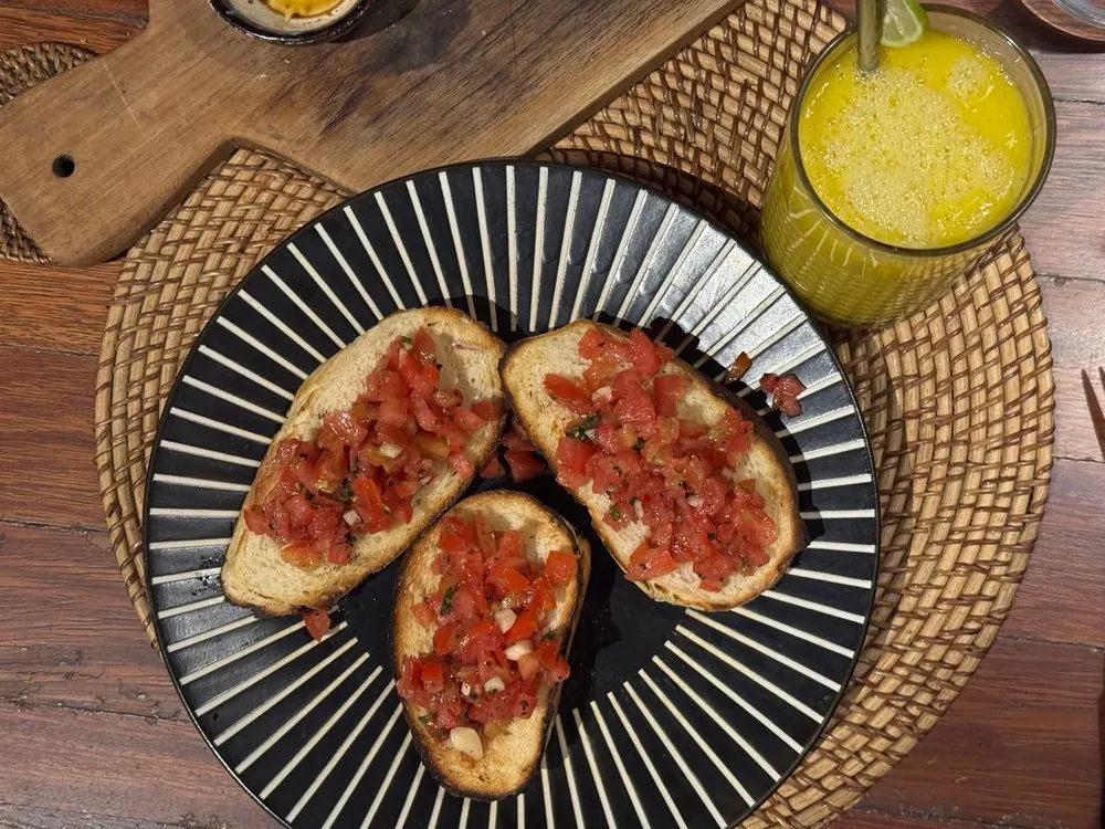 Bruschetta with chopped tomatoes on a black and white striped plate, next to it a yellow drink with a slice of lime