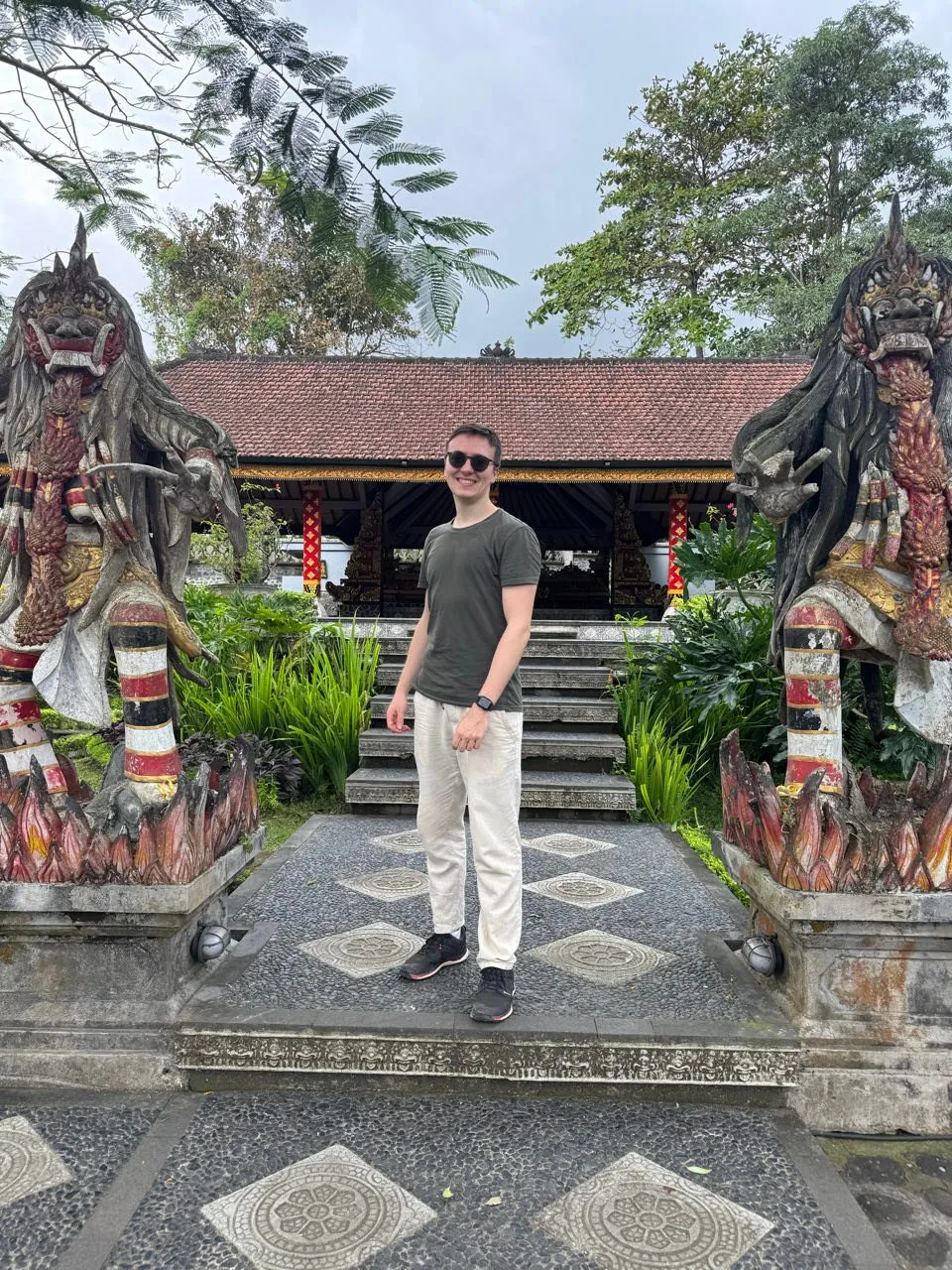 Nicolas stands in front of a staircase to a pavilion, two stone figures with fangs flanking the entrance on the left and right