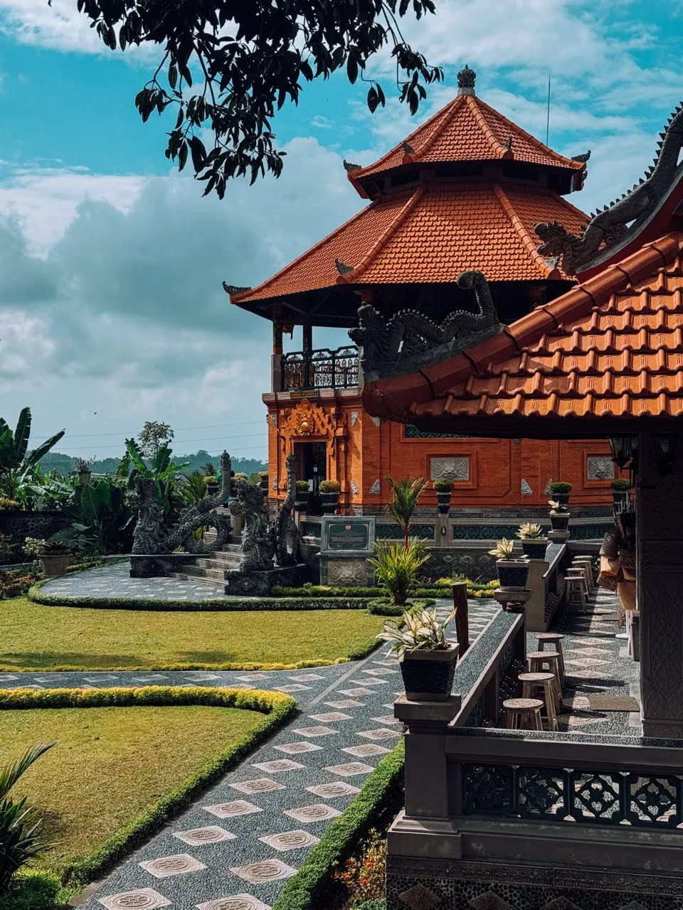 Pavilions with red tiled roofs above a garden with lawns and paths of pebble mosaic
