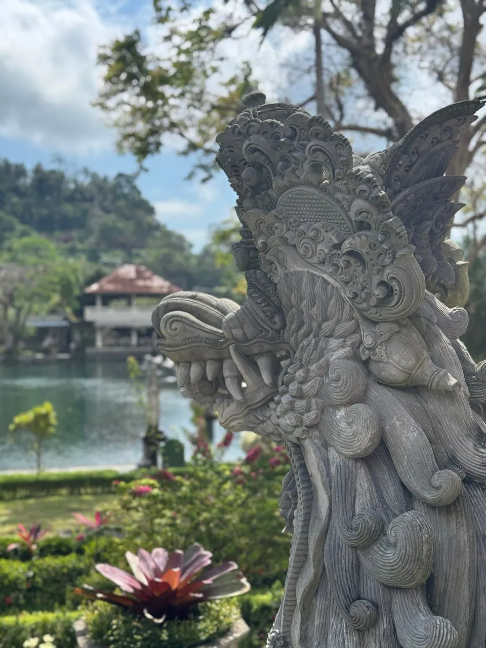 The head of a stone figure with fangs, a pond and a pavilion behind it