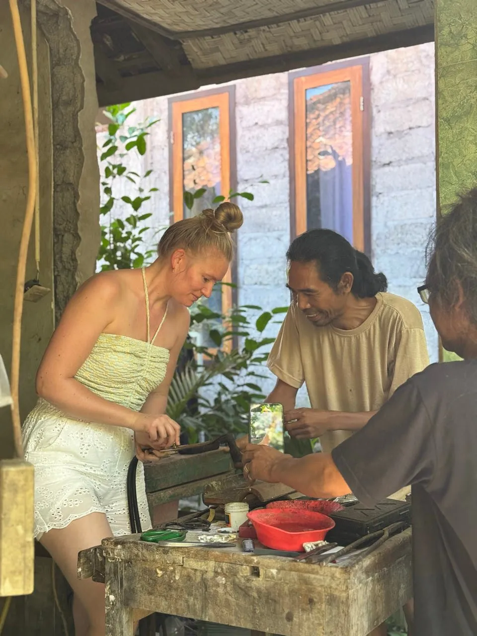 Annina works at a wooden table in the open workshop, a local smiling next to her