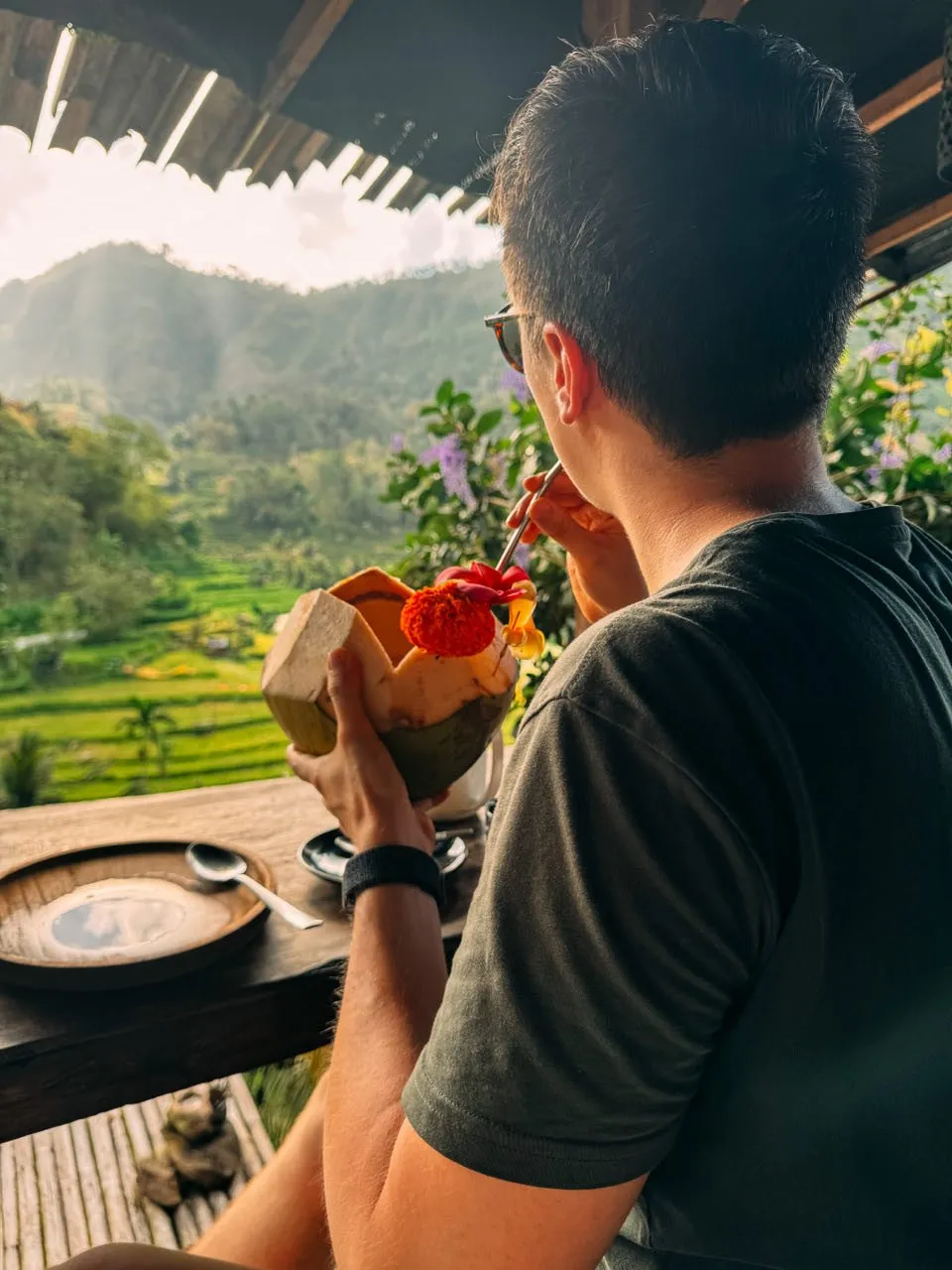 Nicolas drinks from the coconut through a straw, the green terraces behind him in the warm light