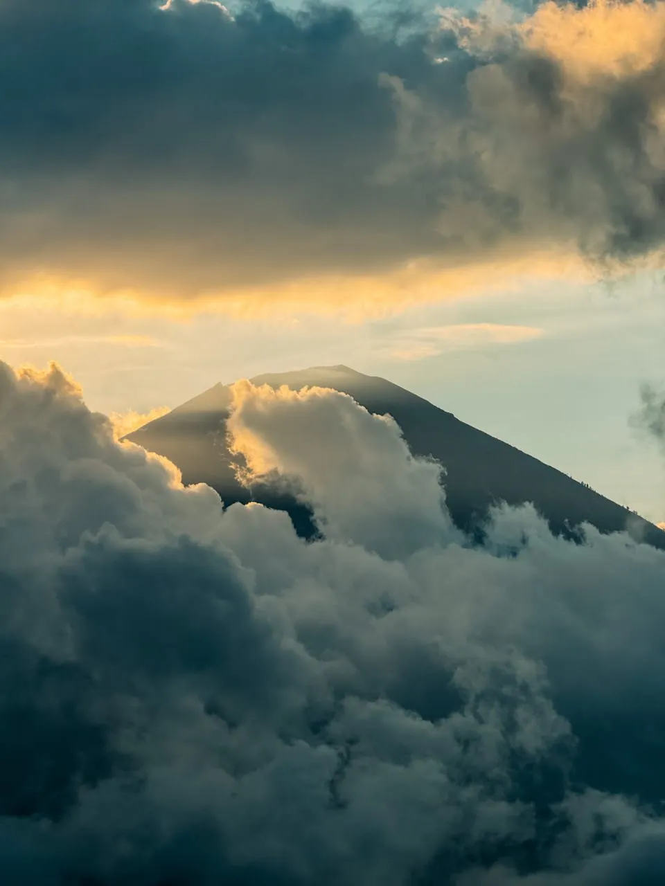 A mountain peak emerges in golden evening light between dark clouds