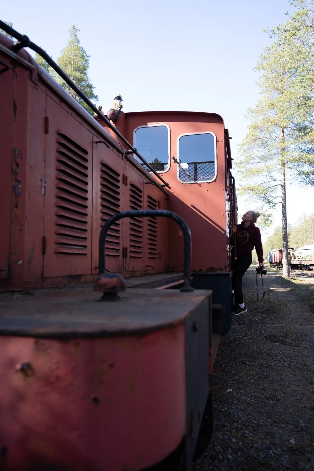 A woman with a camera in her hand looks up along the side of the locomotive, blue sky above