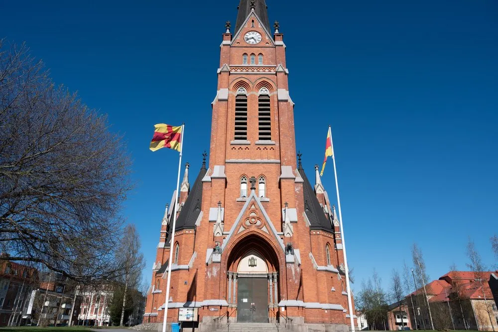 Luleå Cathedral of red brick with a tall tower and two flags waving against a deep blue sky