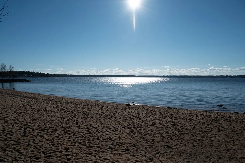 Sandy beach by the water, the sun reflected in the sea