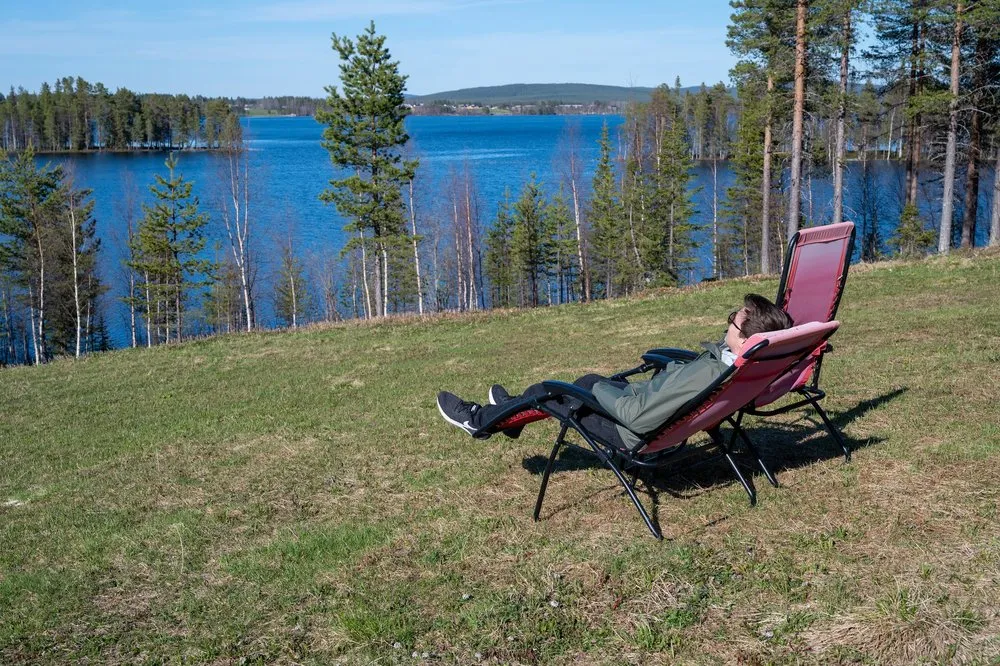 A person lies in the red deckchair on the meadow, looking out over the lake