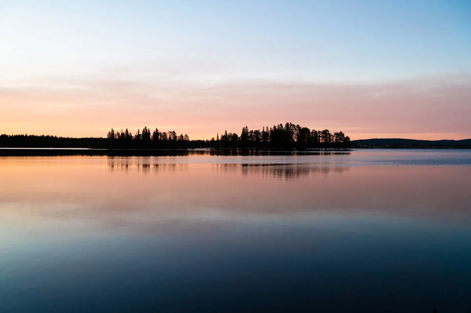 Blasser Abendhimmel in Rosa und Blau, eine bewaldete Landzunge spiegelt sich im ruhigen See