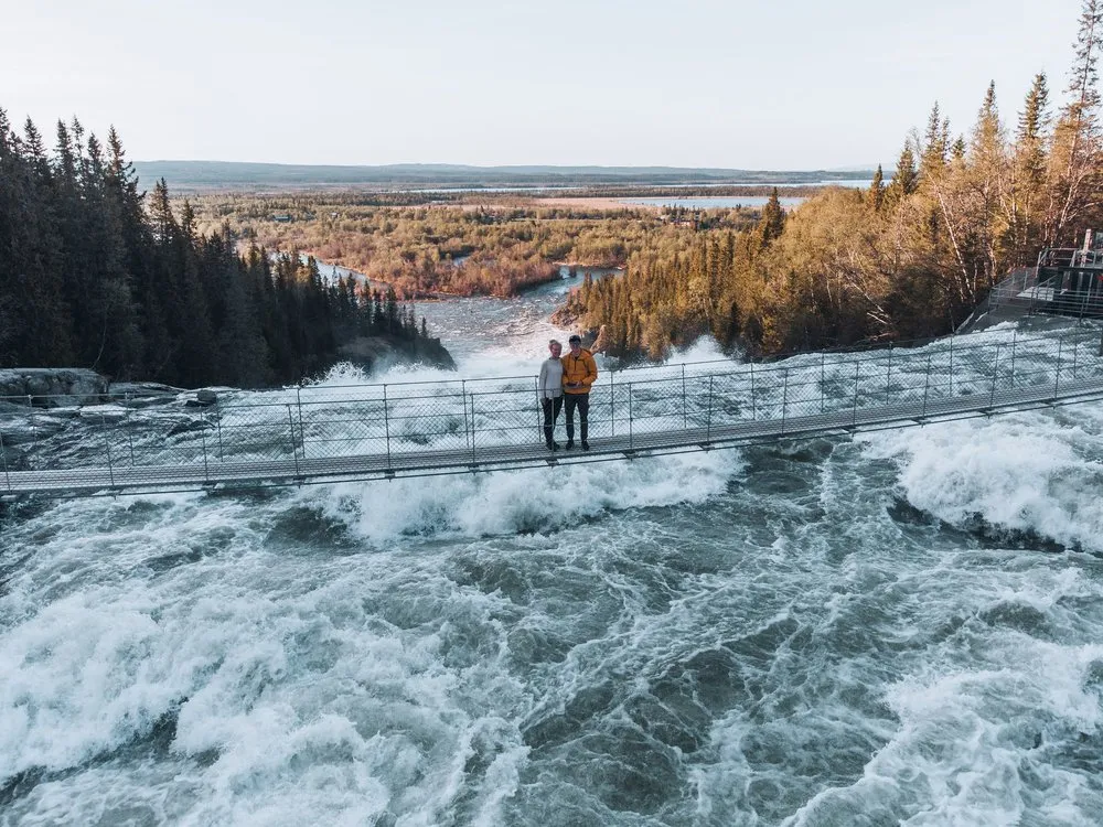 Two people stand on the suspension bridge over the rapids of the Handölsforsen, taken from the air