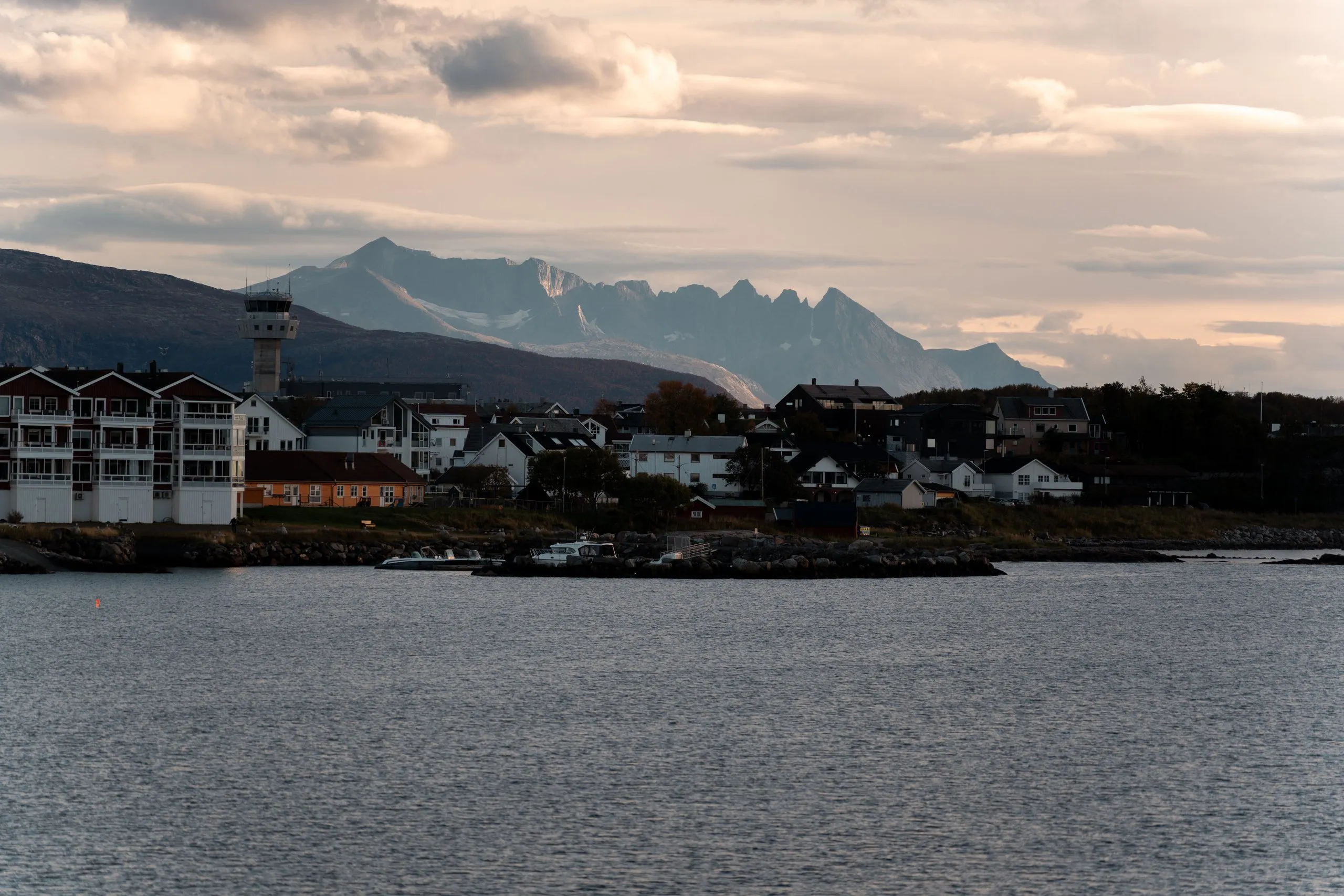 Houses and a tower on the shore in Bodø in the late afternoon light, a jagged mountain range behind them
