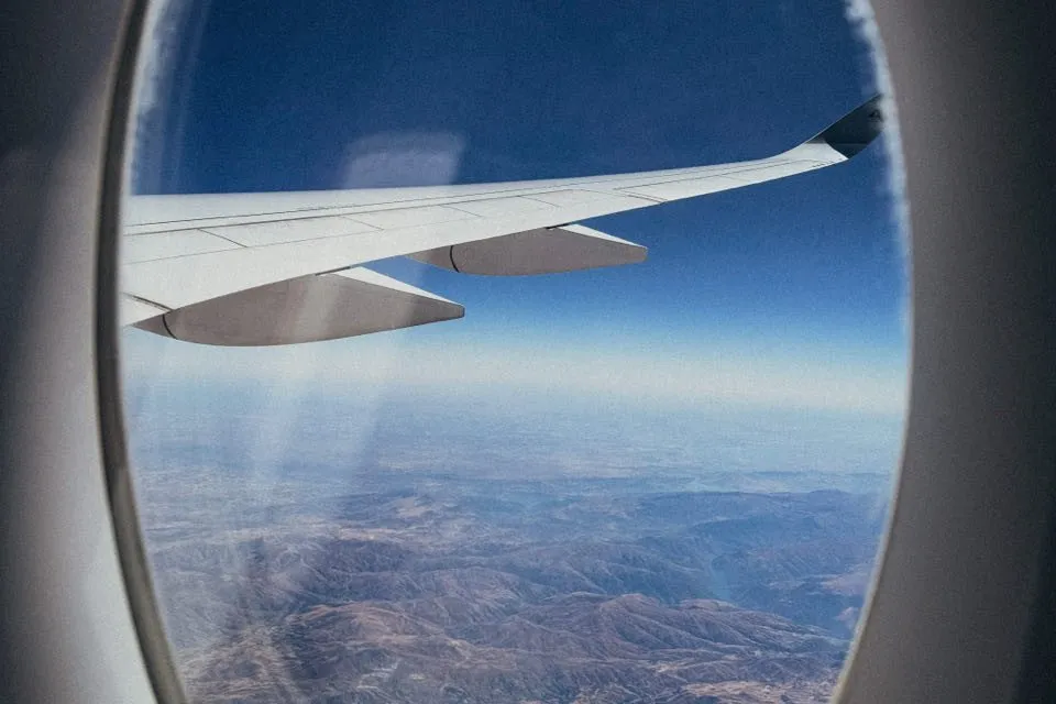 Aircraft wing against a deep blue sky above brown, furrowed mountains