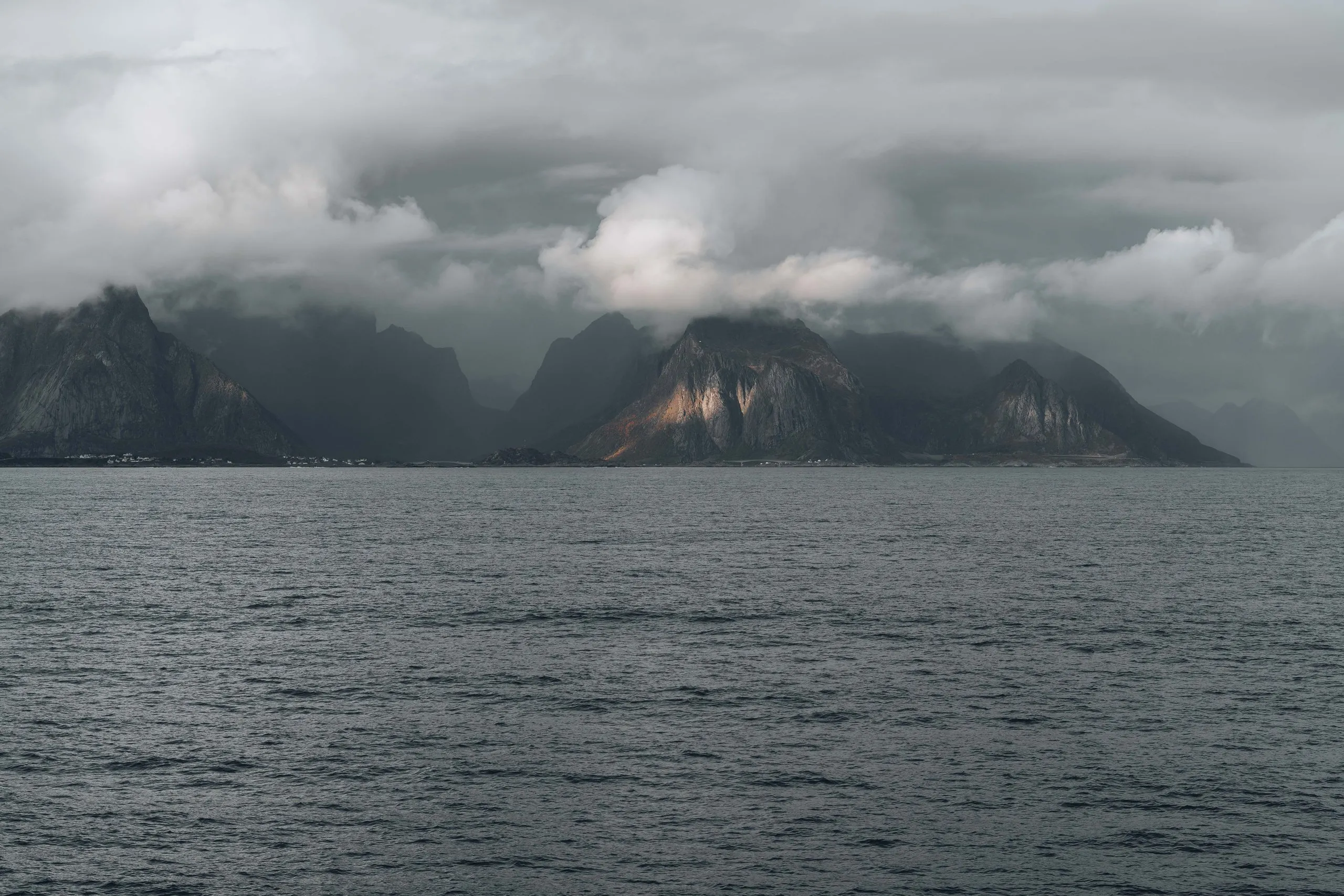 The Lofoten mountains under low clouds, seen from the ferry, one peak catching the light