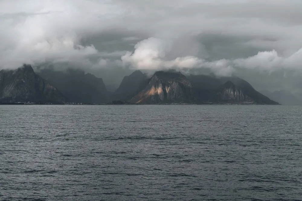 Die Berge der Lofoten unter tiefen Wolken, von der Fähre aus gesehen, ein Gipfel liegt im Licht