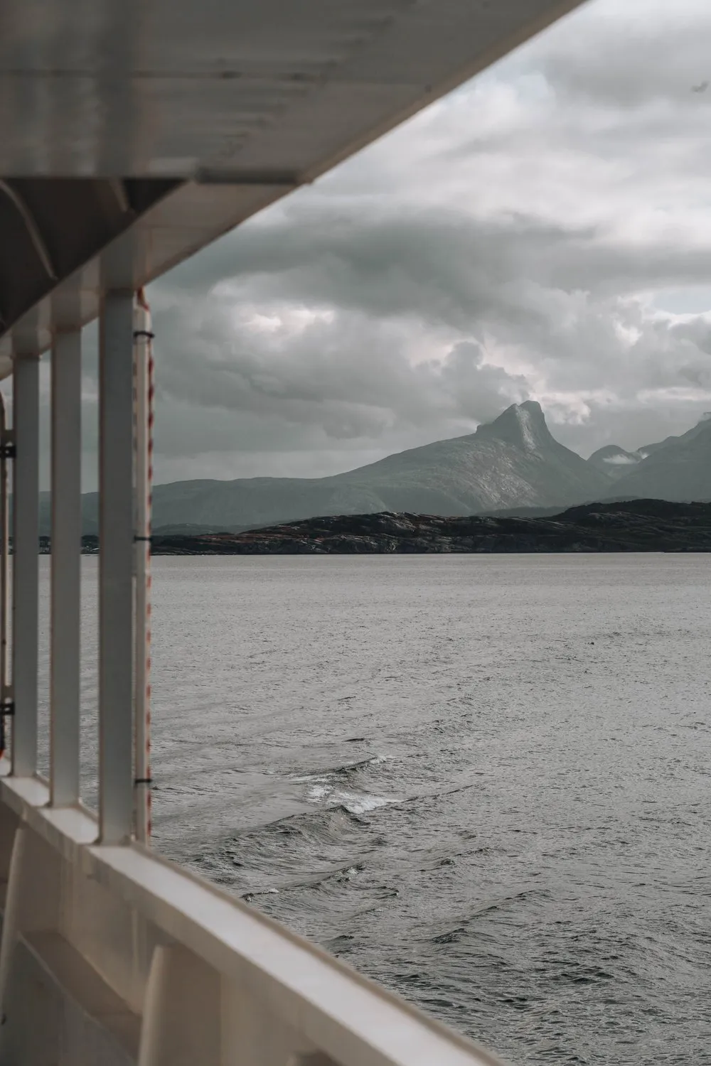 Blick vom Deck der Fähre nach Moskenes auf einen spitzen Berg über dem grauen Meer