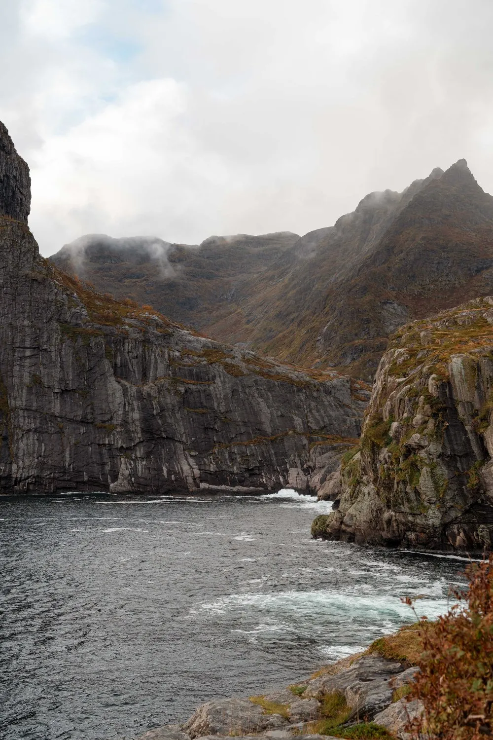 Steile Felswände und das offene Meer am äussersten Rand von Å, die Berge in den Wolken