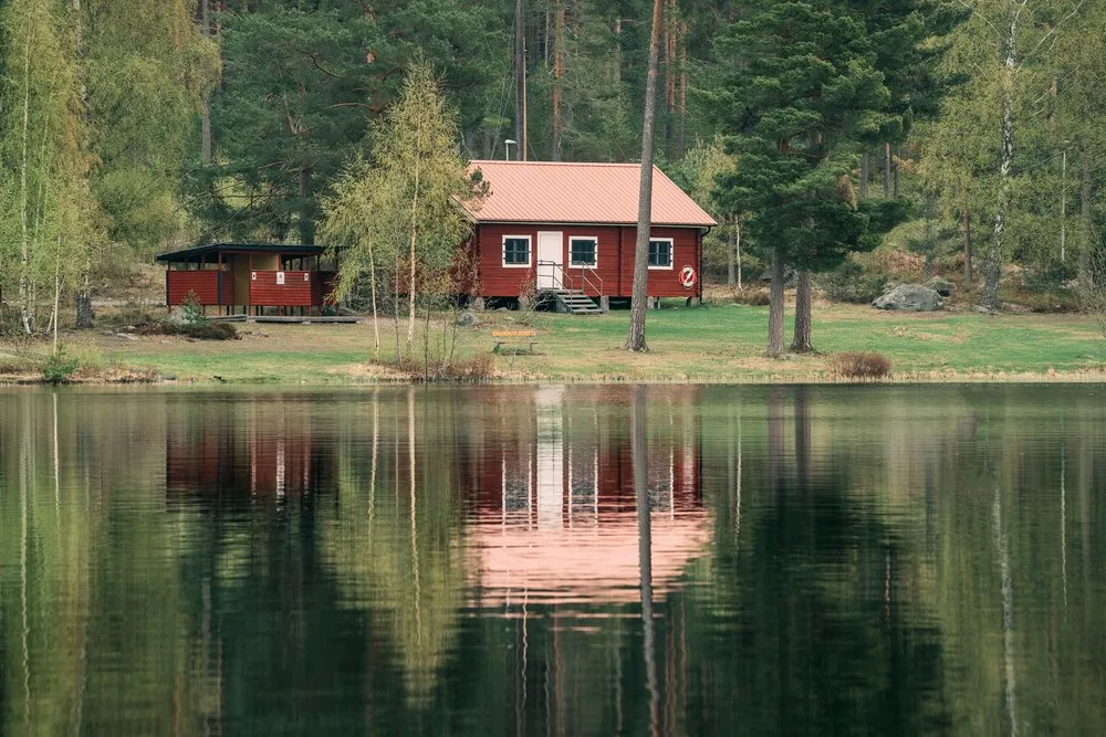 Rotes Holzhaus am Ufer eines Waldsees, das sich im stillen Wasser spiegelt
