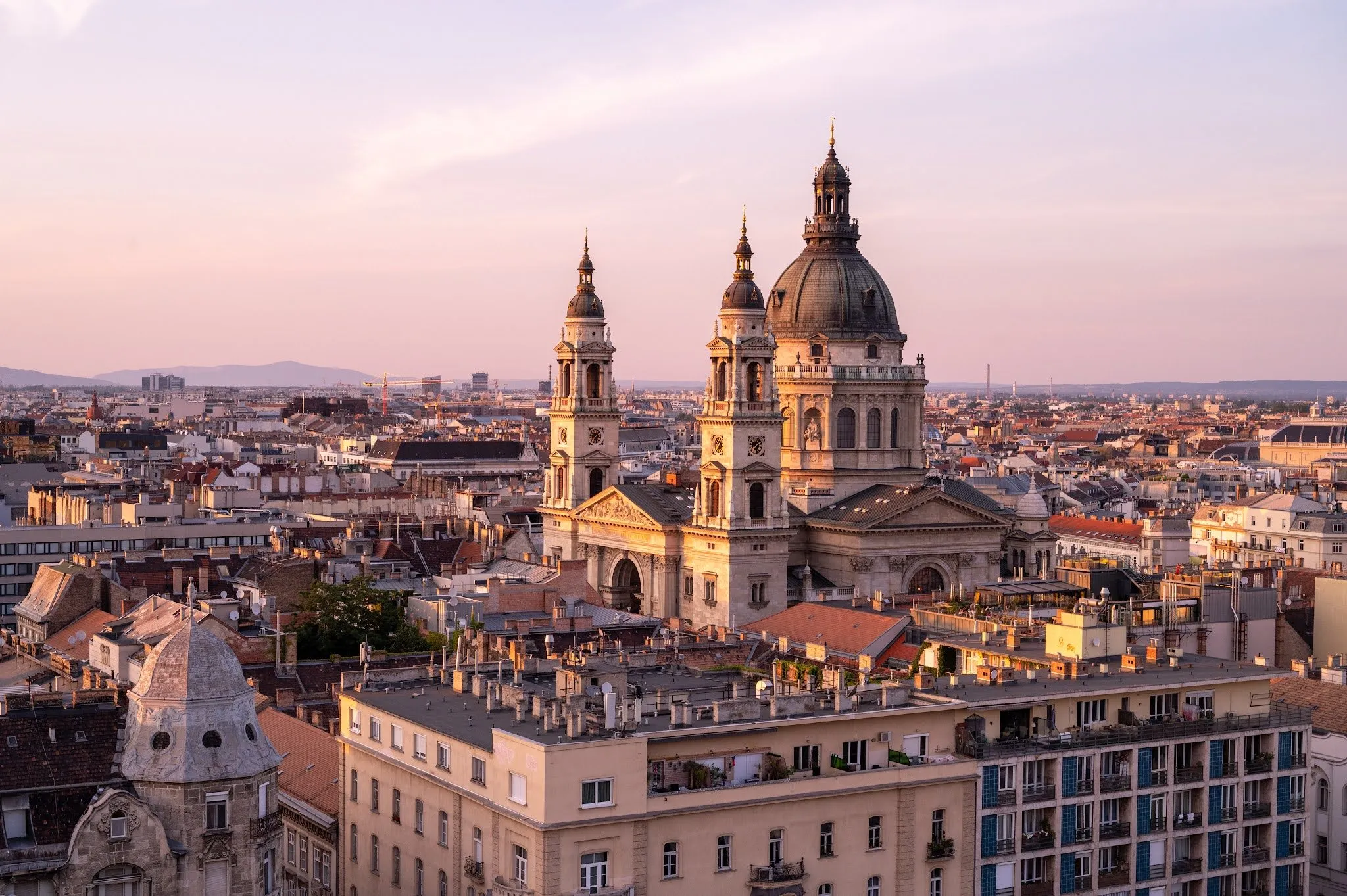 View across the rooftops of a basilica with a dome and two towers in pink evening light