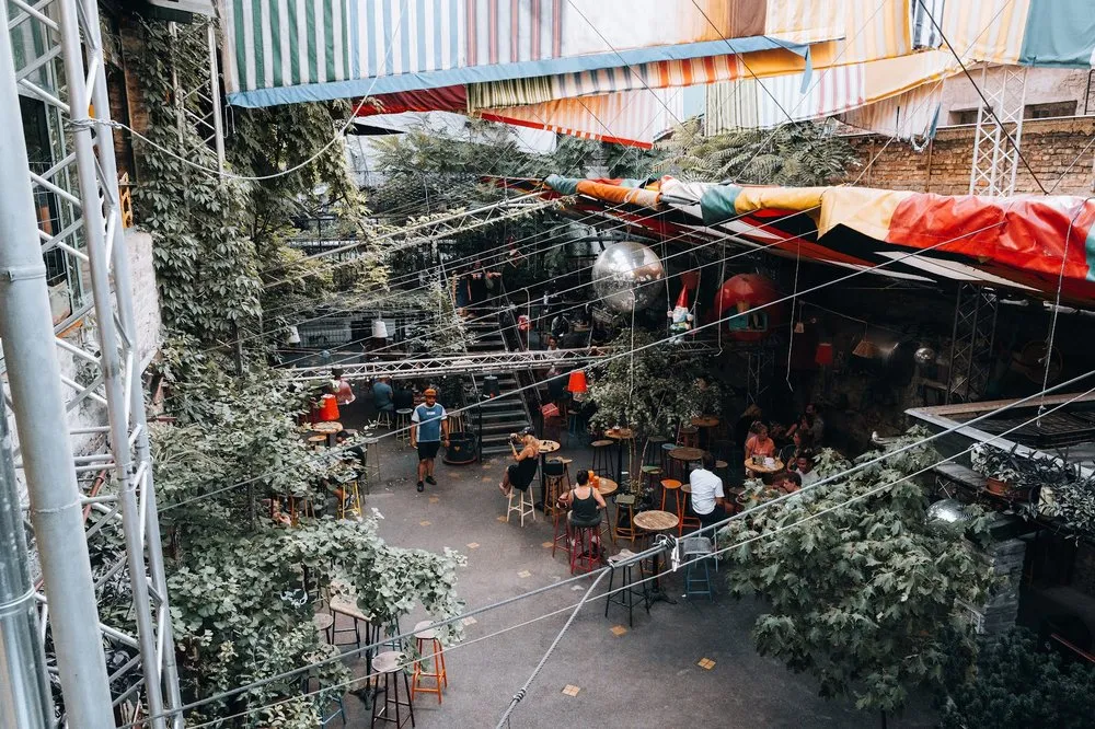 Looking down into the courtyard of the ruin bar, with tables, stools and colourful tarpaulins under climbing plants