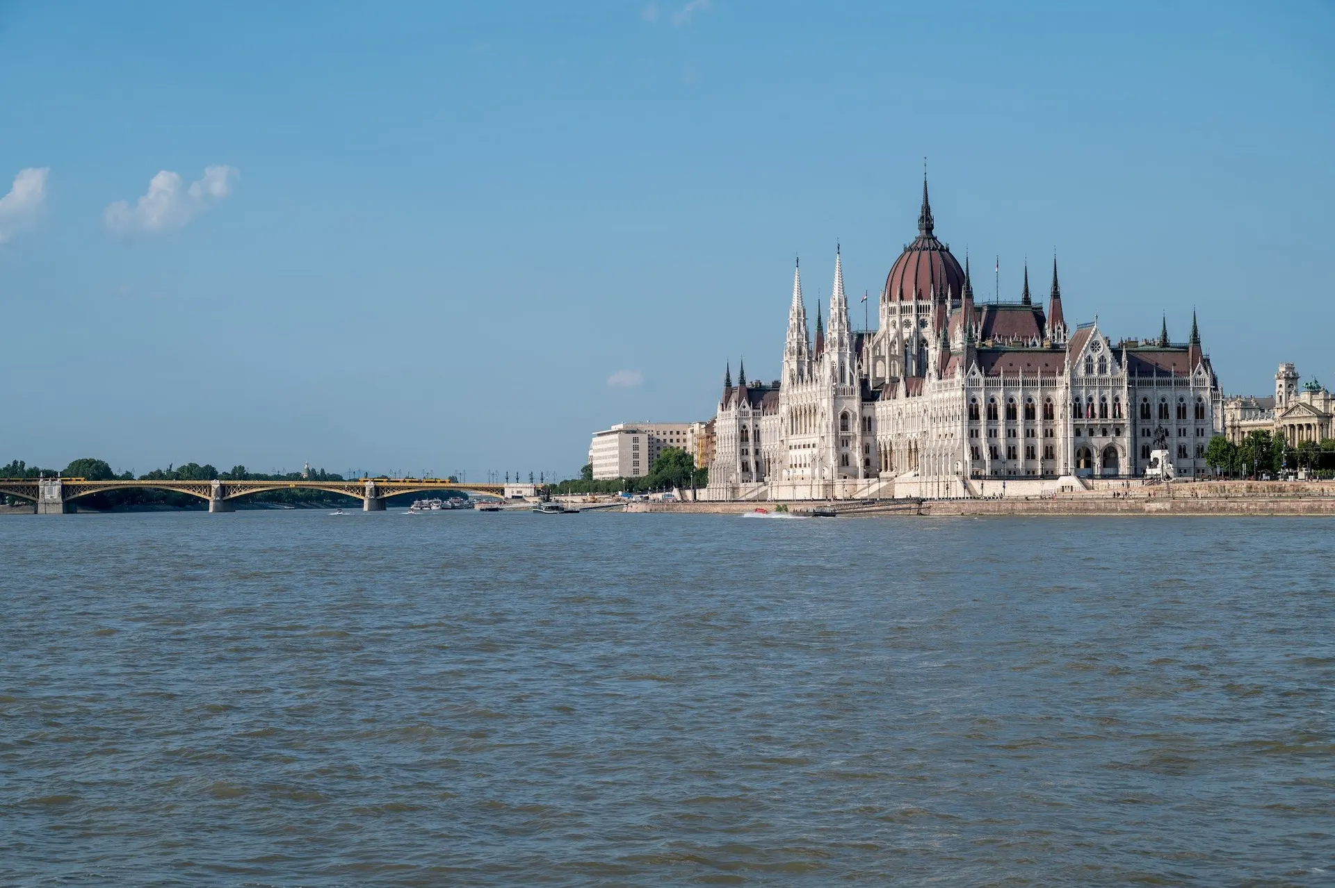 View across the Danube of a white building with a red dome and pointed towers on the bank, a bridge on the left