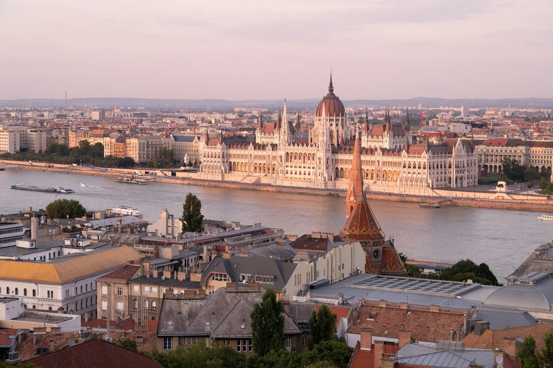 View over rooftops and the Danube to a long domed building on the bank of the Pest side in warm evening light