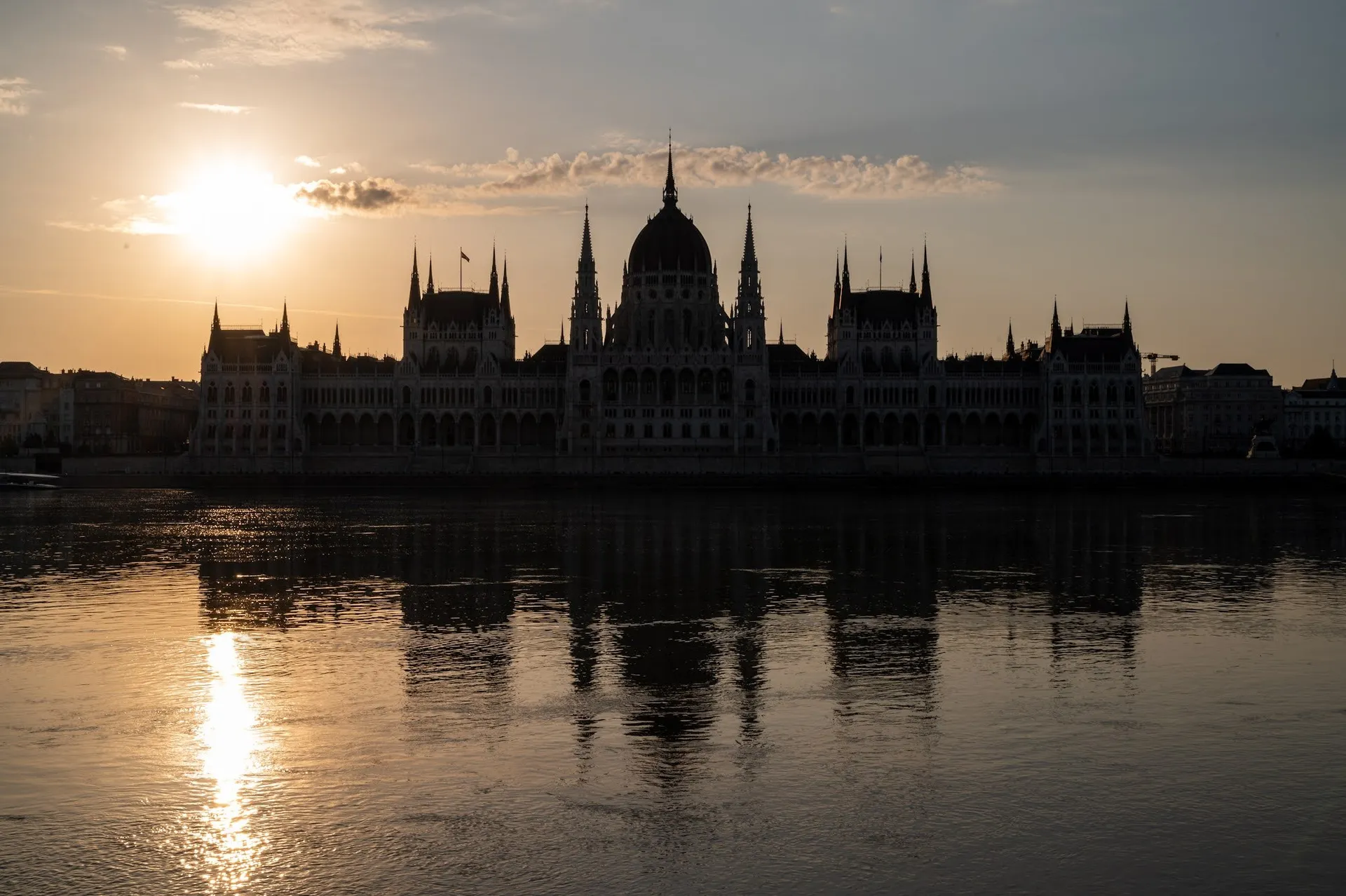 The Parliament as a silhouette in the red of dawn, on the left the rising sun and its reflection in the Danube
