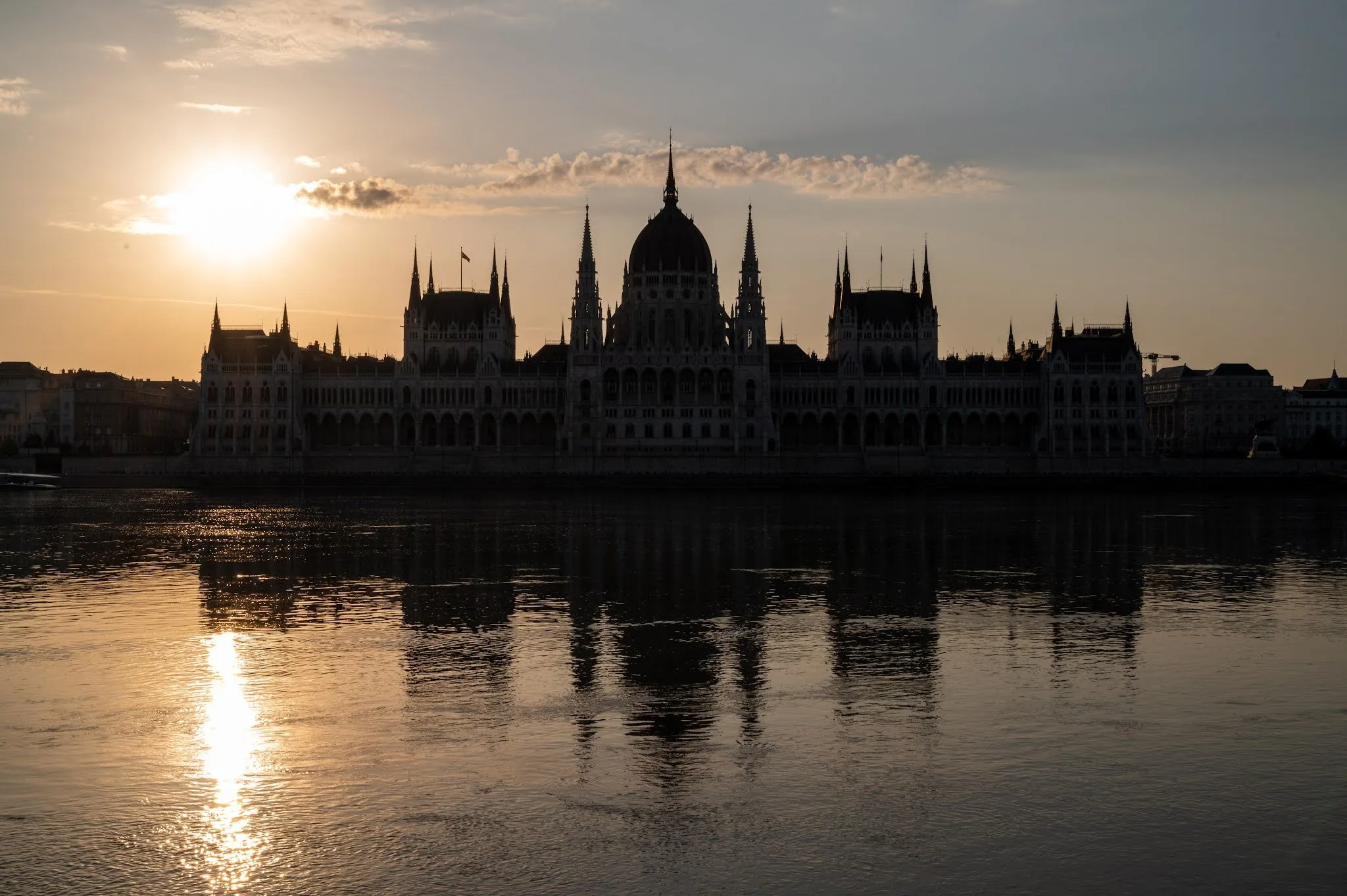 The Parliament as a silhouette in the red of dawn, on the left the rising sun and its reflection in the Danube