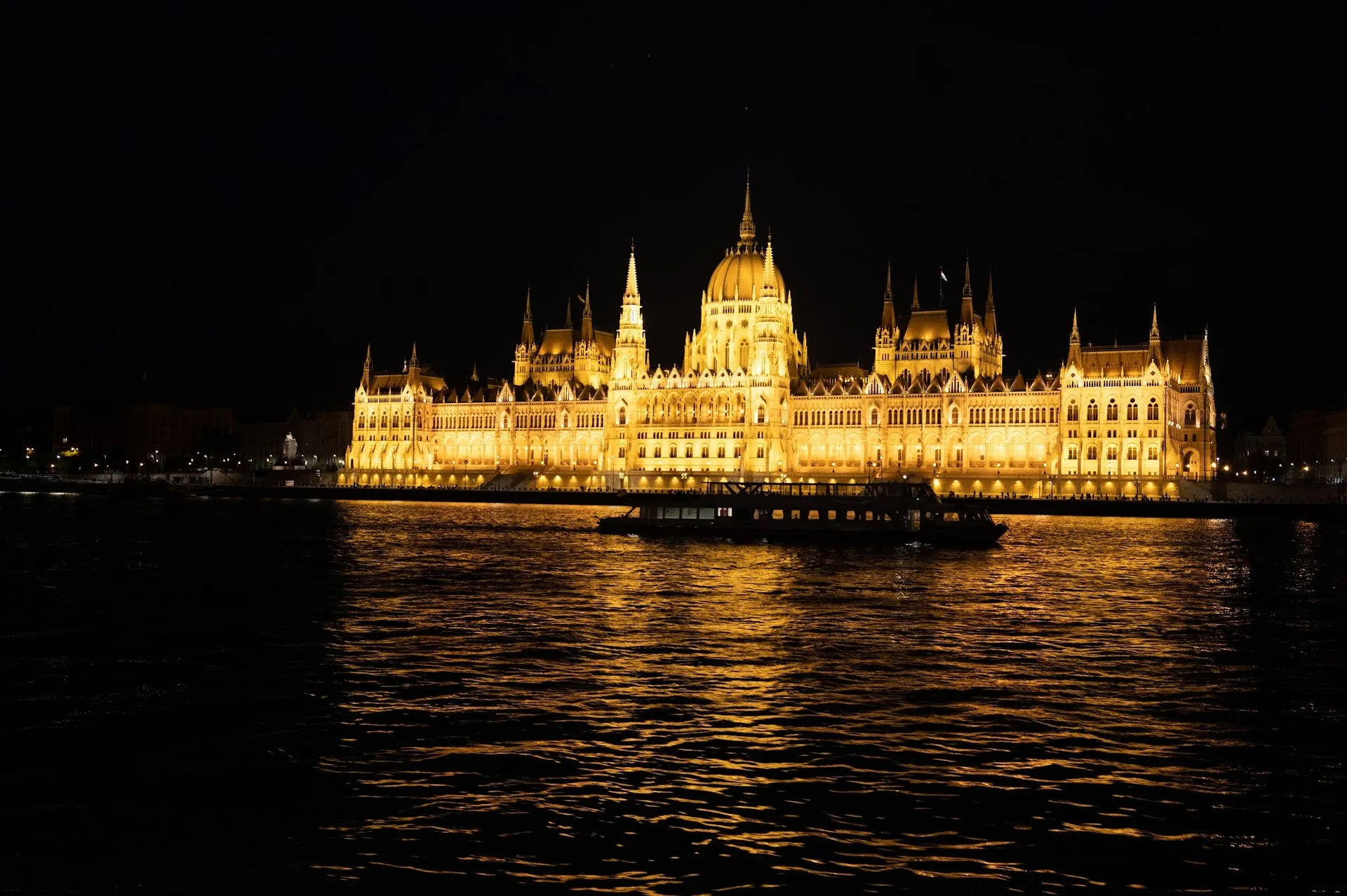 The Parliament at night, lit in yellow on the bank of the Danube, in front of it a ship on the dark water