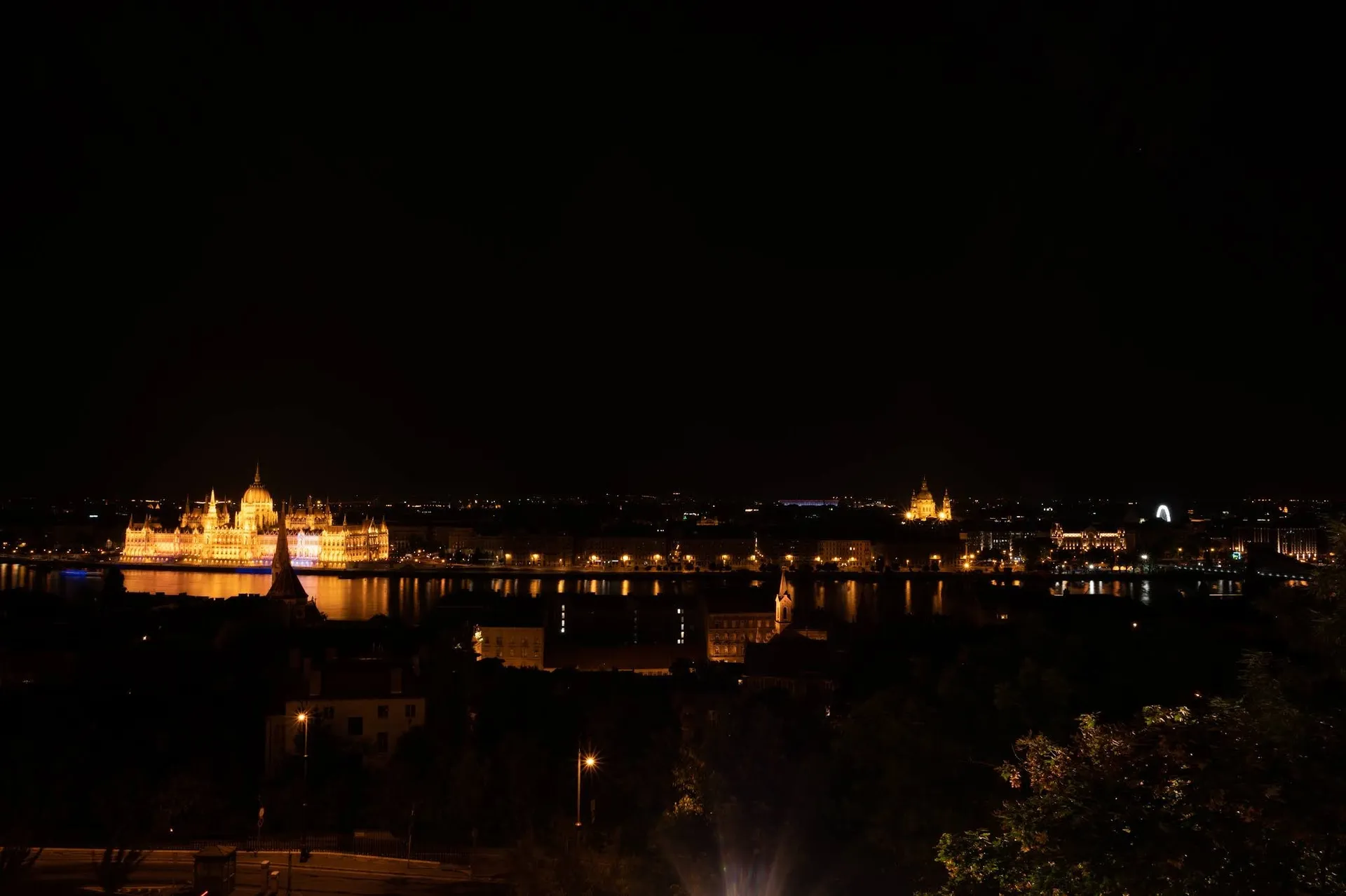 Night shot from above over the dark river, on the opposite bank a building with a dome glows beside more lights