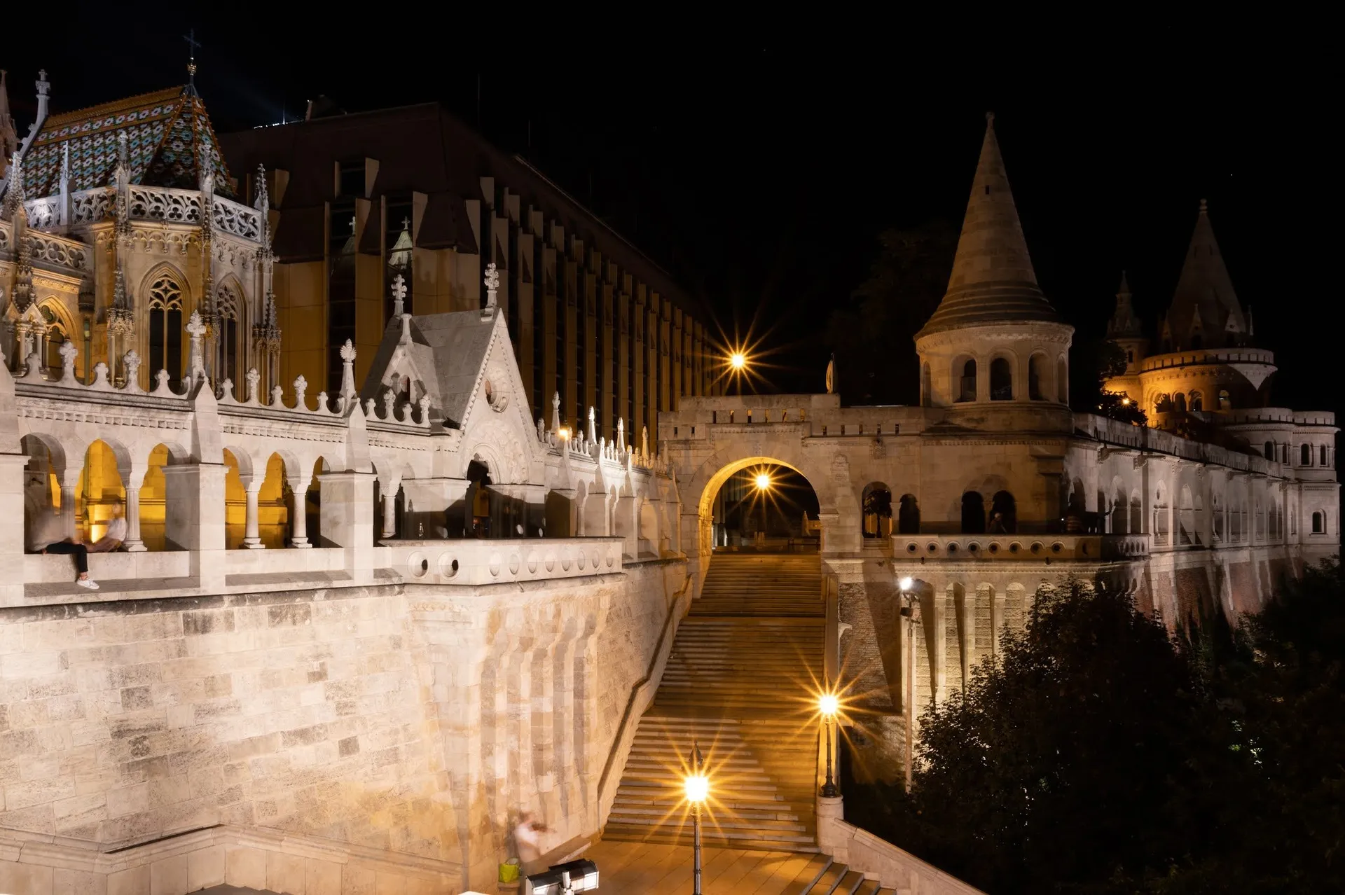 Fisherman's Bastion at night with a lit staircase and archway, on the left the lit-up church
