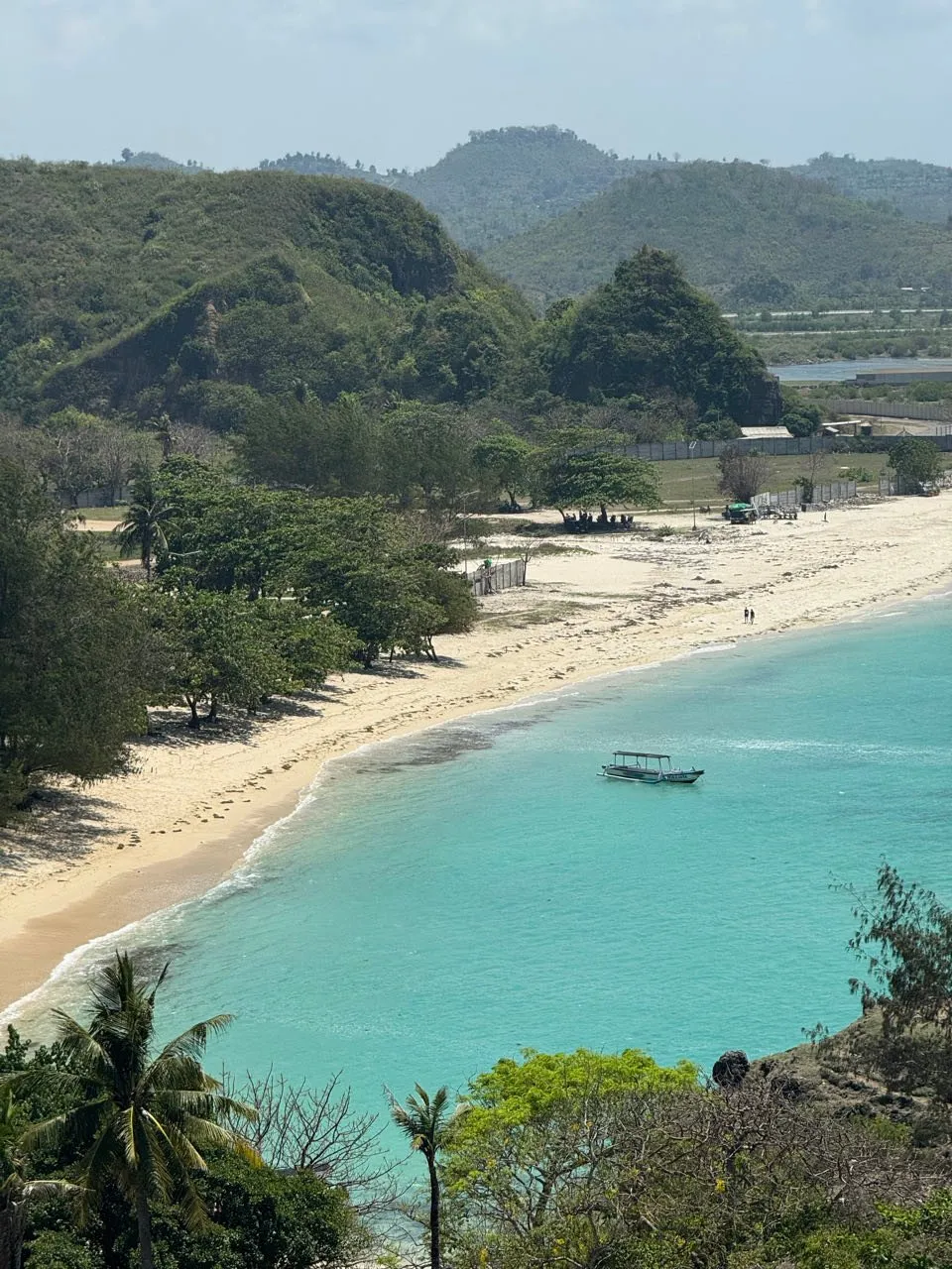 Blick vom Bukit Merese auf eine Bucht mit hellem Sandstrand, dahinter grüne Hügel