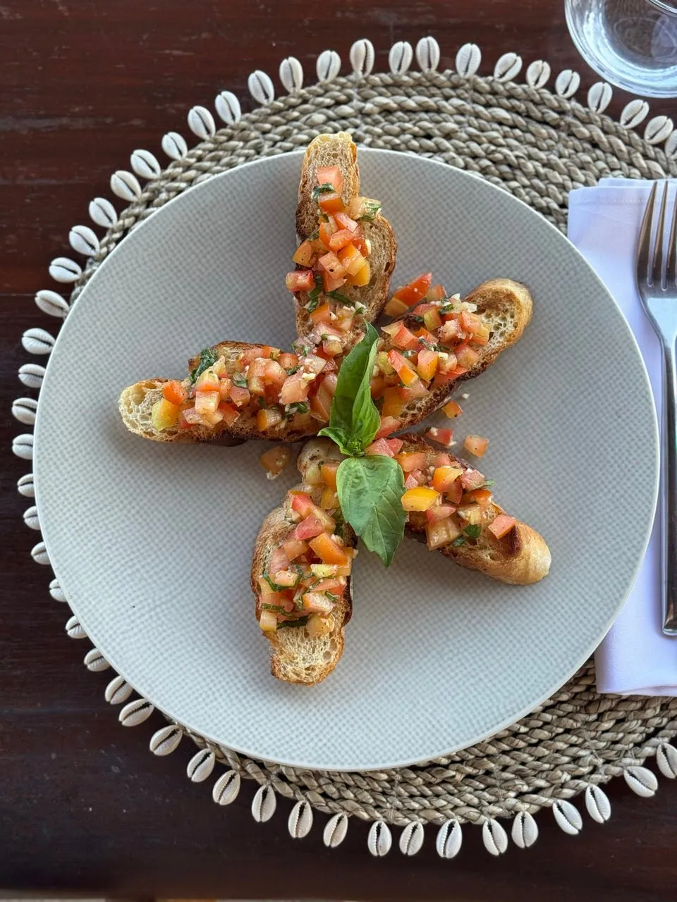 Five bruschetta with chopped tomatoes and a basil leaf, arranged in a star shape on a light plate