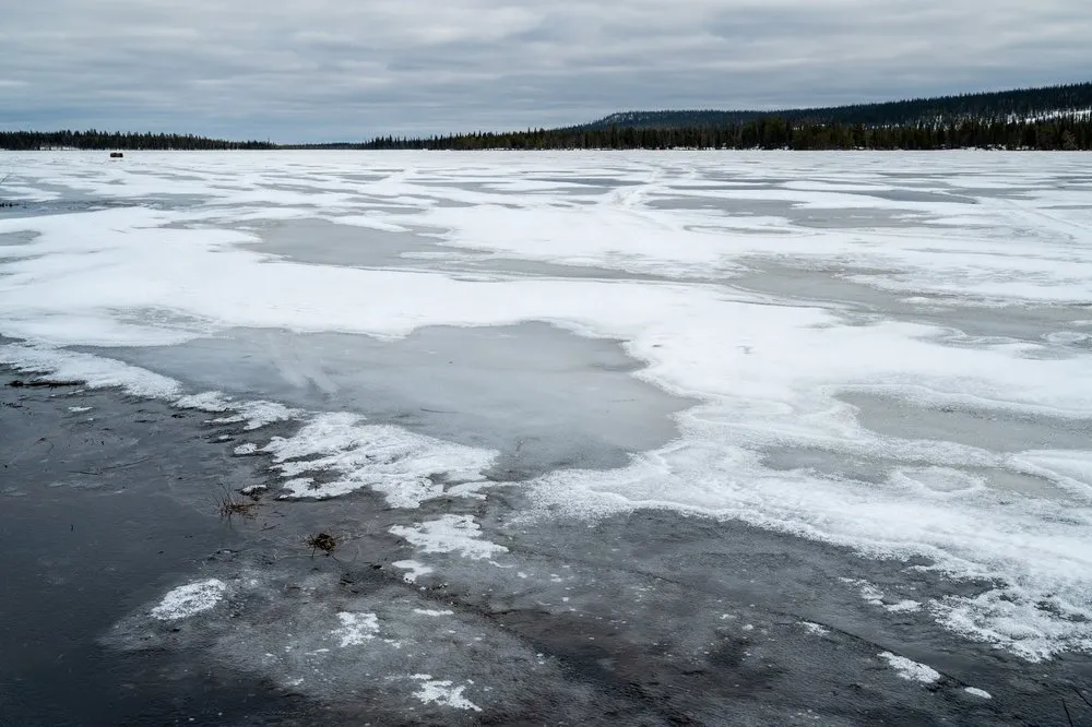 Halt an einem zugefrorenen See auf der Fahrt nach Jokkmokk, graues Eis mit Schneeflecken, am Ufer gegenüber Nadelwald