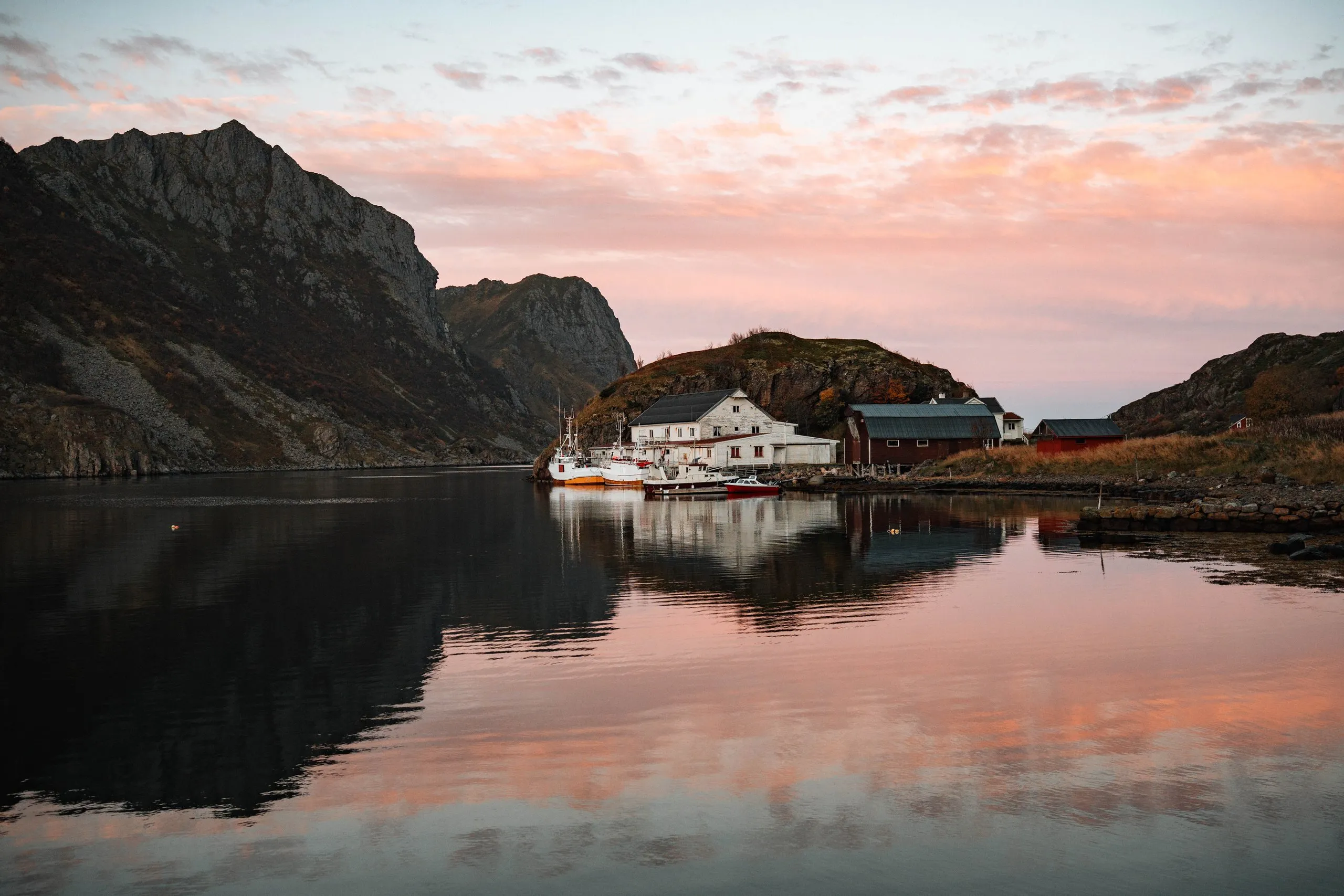 Sonnenaufgang über der stillen Bucht von Straumsjøen, Häuser, Boote und Berge spiegeln sich im rosa Wasser