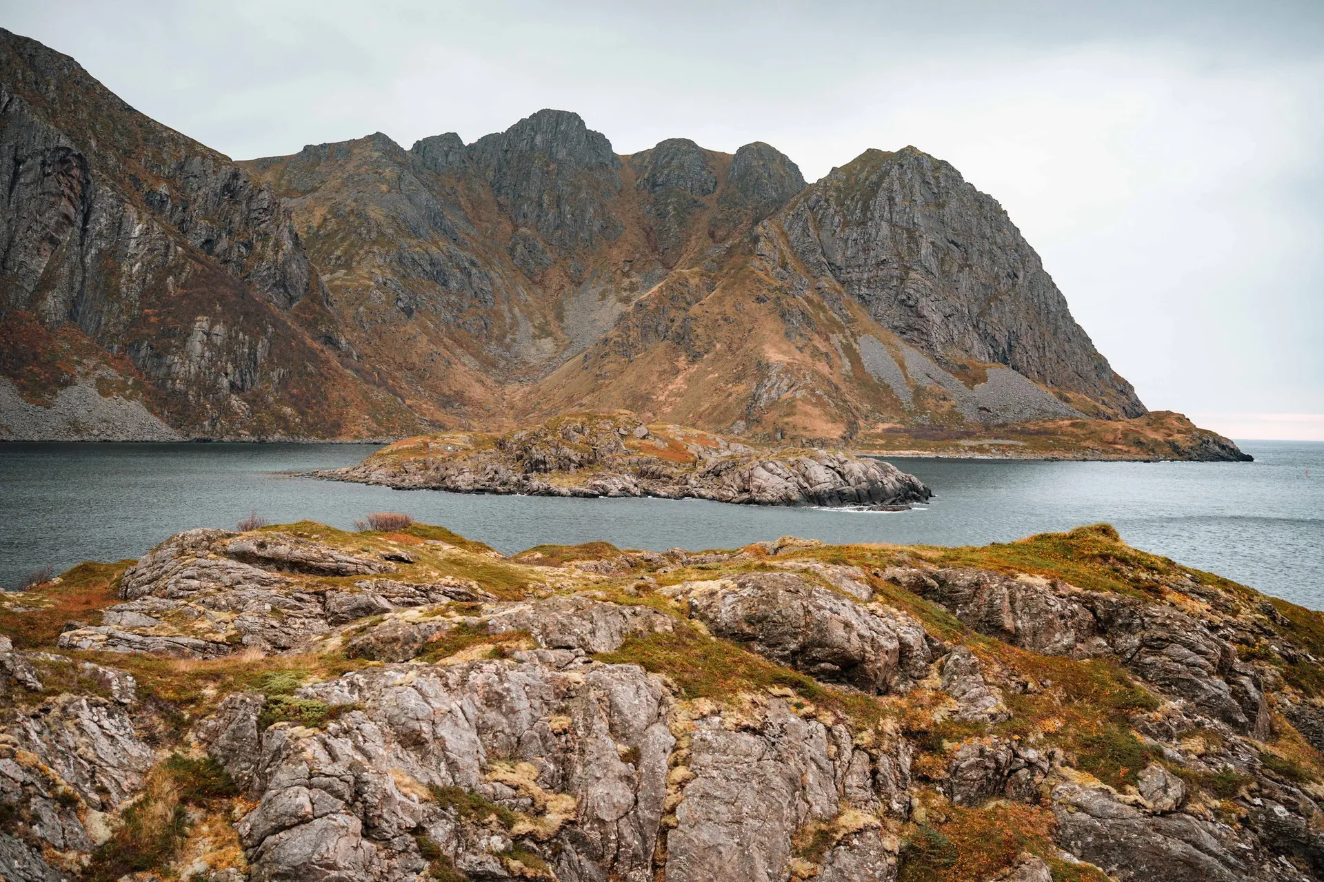 Eine kleine Felsinsel in der Bucht vor einer Kette steiler Berge, vom Coastal Trail bei Straumsjøen aus