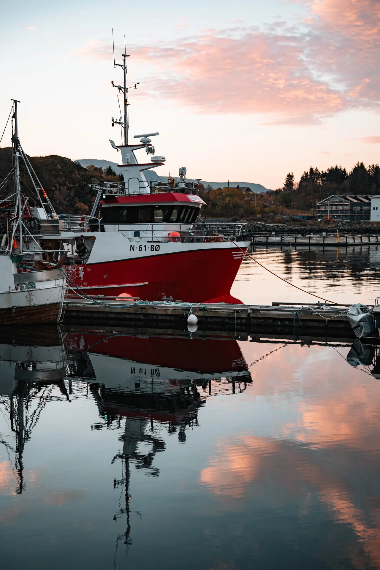 Ein rot-weisses Fischerboot am Kai in Straumsjøen, das sich mit den rosa Wolken im stillen Wasser spiegelt
