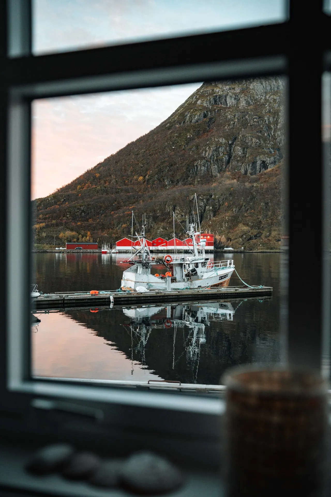 Blick aus dem Fenster auf Fischerboote im Hafen von Straumsjøen und einen Berg im Morgenlicht
