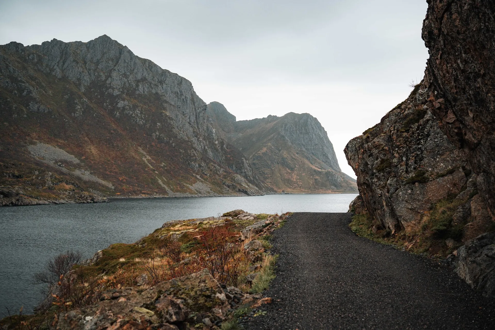 Der Kiesweg des Coastal Trail zwischen einer Felswand und dem Wasser, dahinter steile Berge