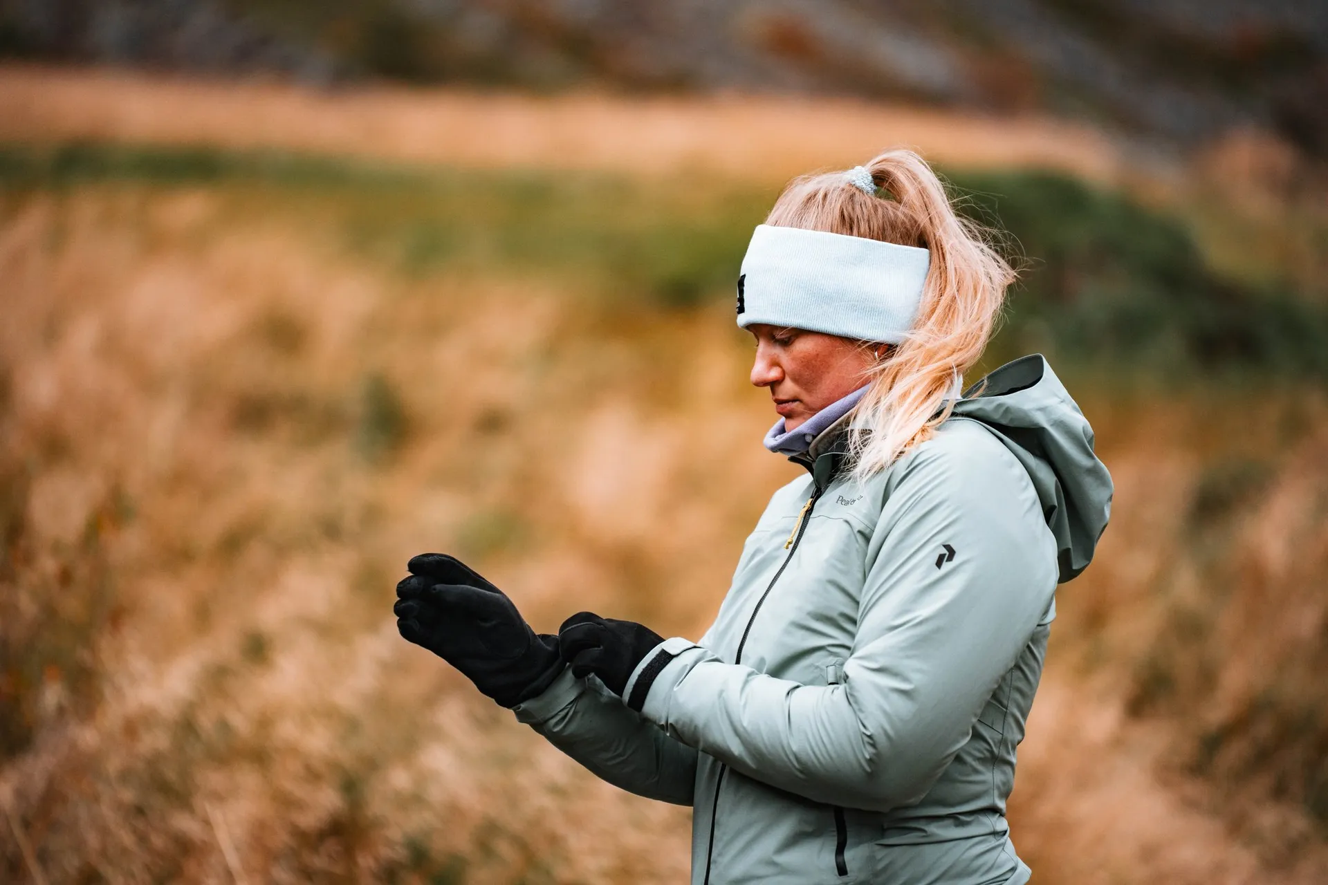 Annina mit Stirnband und Handschuhen im Wind, hinter ihr unscharf das goldene Gras