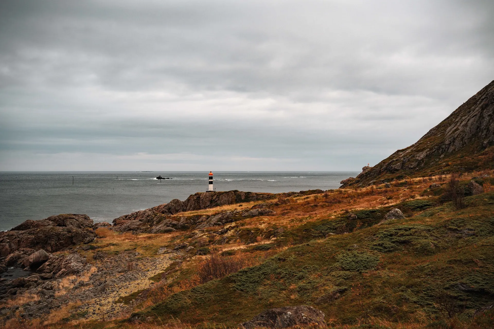 Der kleine weisse Leuchtturm mit schwarzen Bändern und rotem Dach bei Vikan auf den Felsen am Meer, darüber ein grauer Himmel