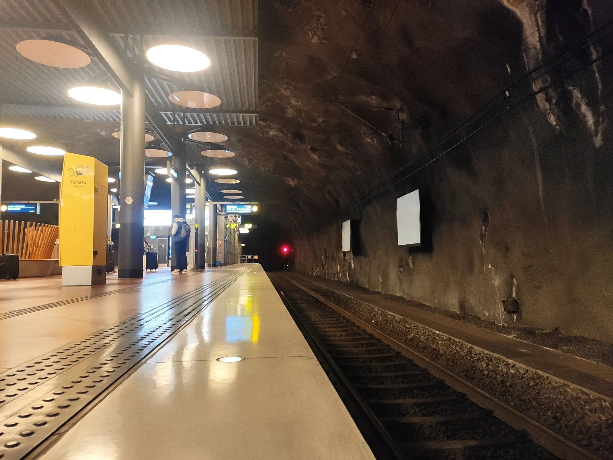 Almost empty Arlanda Express platform in a rock tunnel, a yellow pillar and a person with a backpack in the background