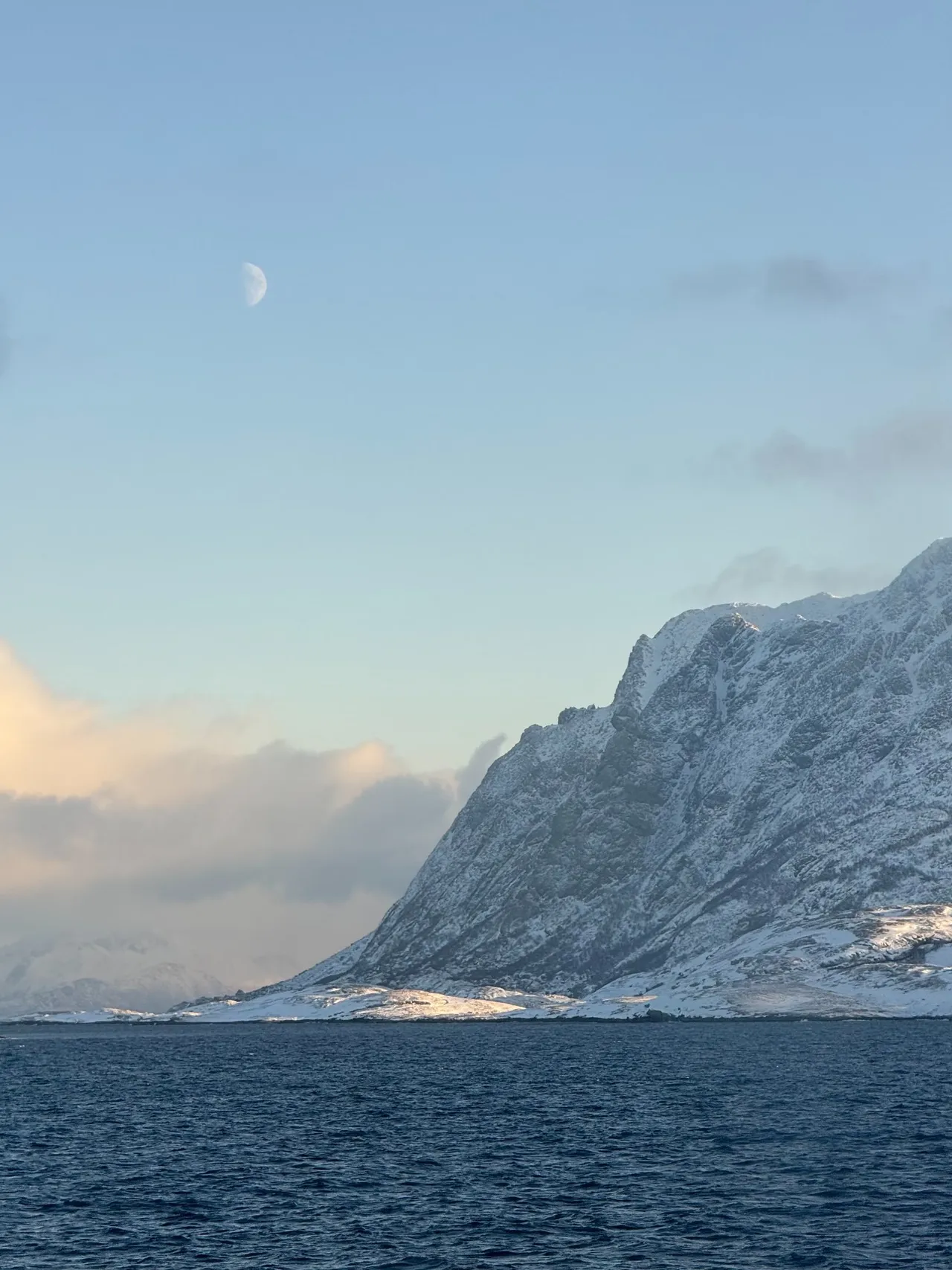 The moon above a snowy mountainside on the fjord