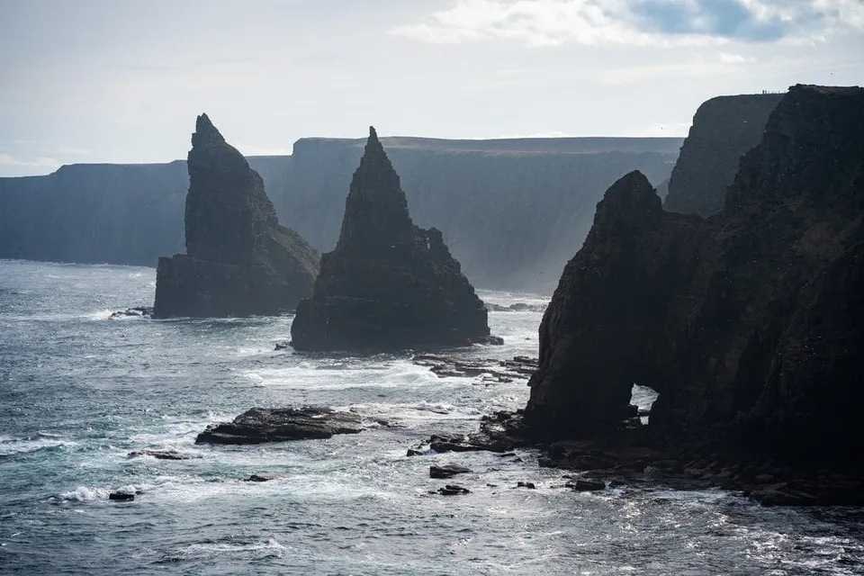 Die Felsnadeln von Duncansby im Gegenlicht, rechts ein Felsentor in der Klippe