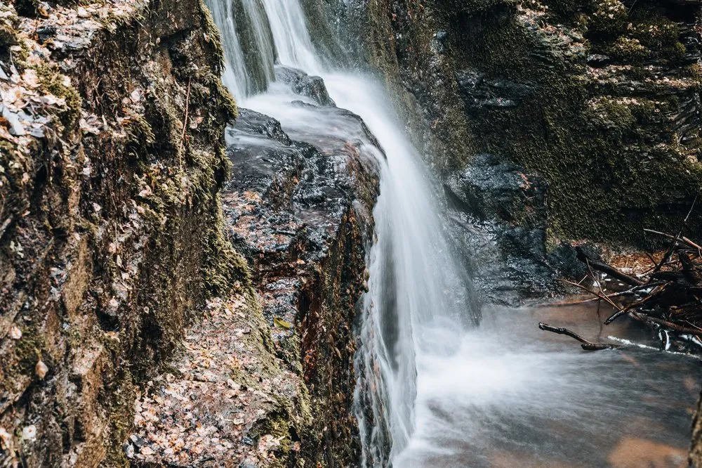 Nahaufnahme eines Wasserfalls, der über eine dunkle Felskante in ein flaches Becken fliesst