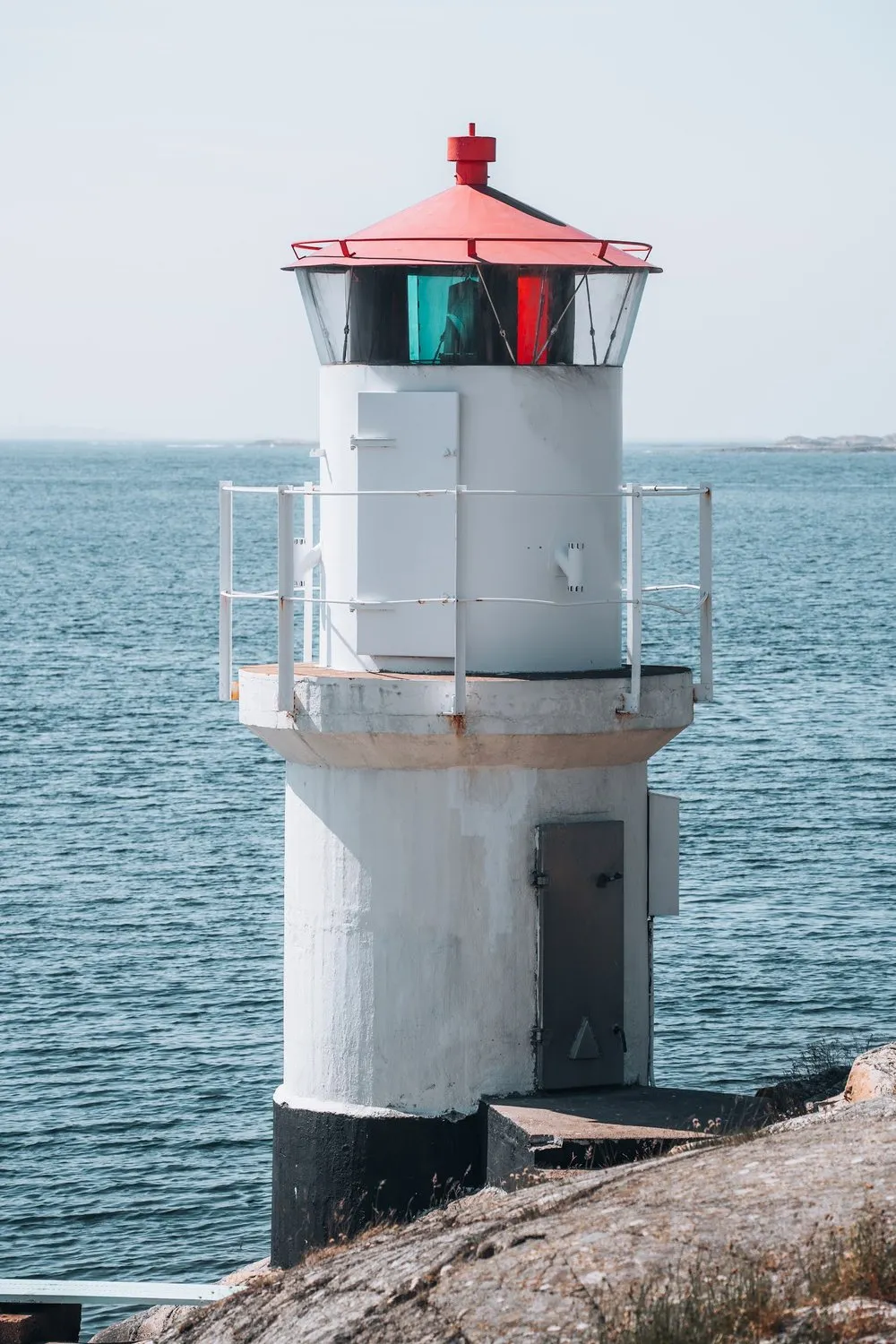 Close-up of the white lighthouse with a red roof and green and red panes in the lantern