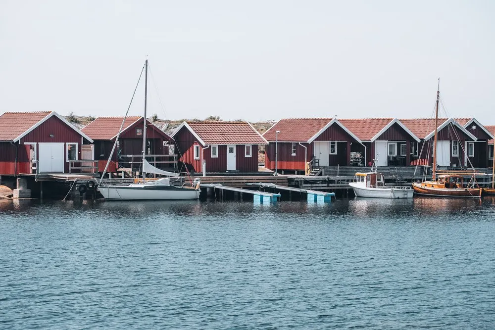 Dark red boathouses on a jetty, sailing boats and a motorboat on the smooth water in front
