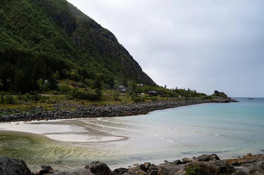 Light sandy beach with turquoise water at Rørvikstranda, a wooded slope with a few houses on the left