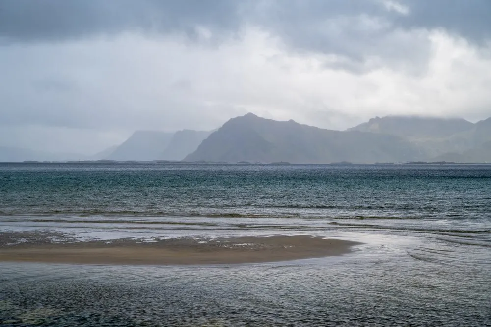 Flat sandbank in the water, mountains in the rain haze behind it