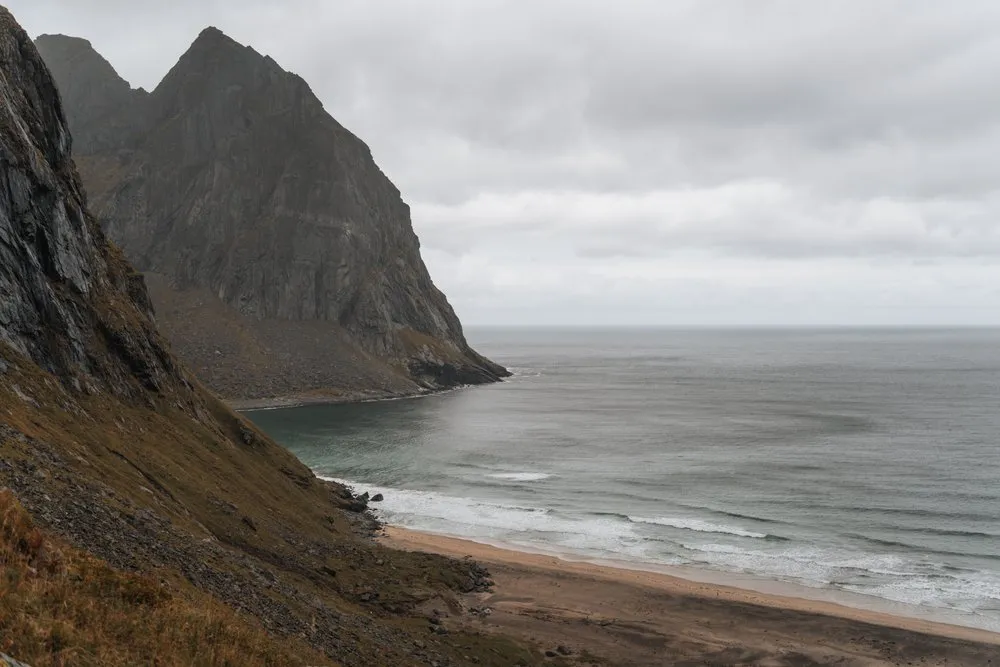 Blick von oben auf die Bucht von Kvalvika, zwischen steilen Felswänden rollen die Wellen auf den Sand