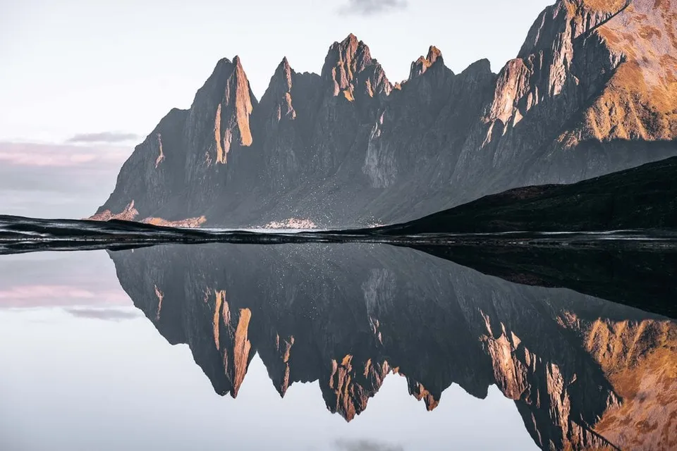 Die Zacken der Okshornan bei Tungeneset im rosa Morgenlicht, vollständig im stillen Wasser gespiegelt